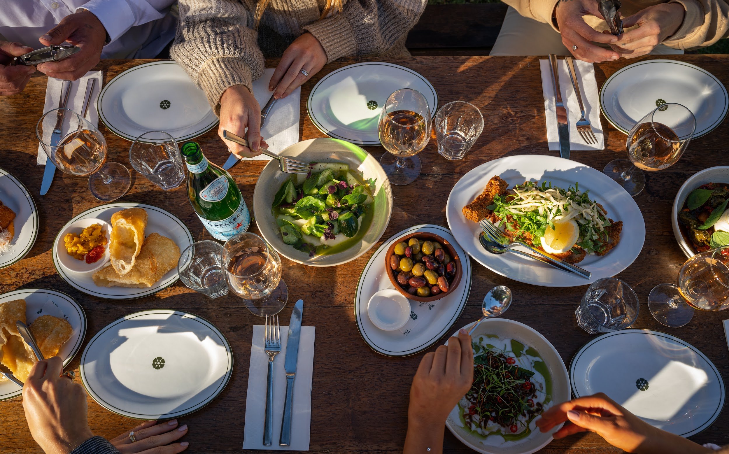 Overhead view of a shared long lunch with salads, olives and wine at Lost Phoenix Farm