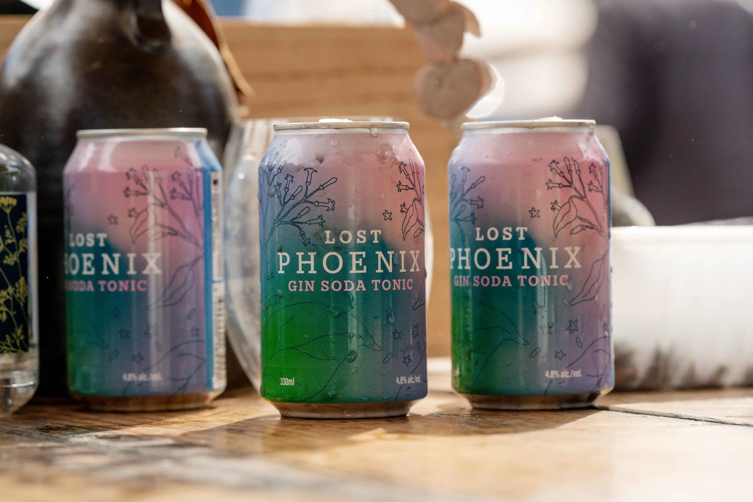 Cans of Lost Phoenix Gin Soda Tonic on a timber table