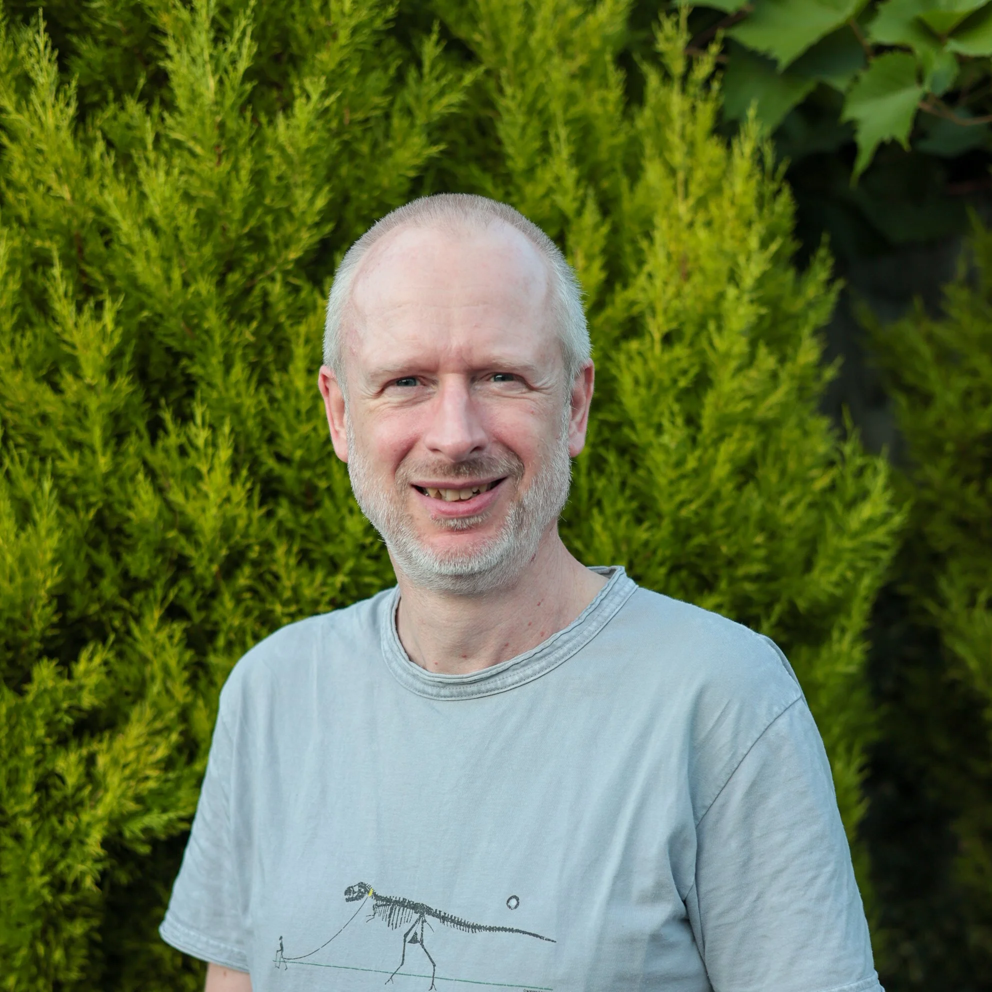 Man wearing a black cap and T-shirt with yellow text, standing outdoors near boats and a marina.