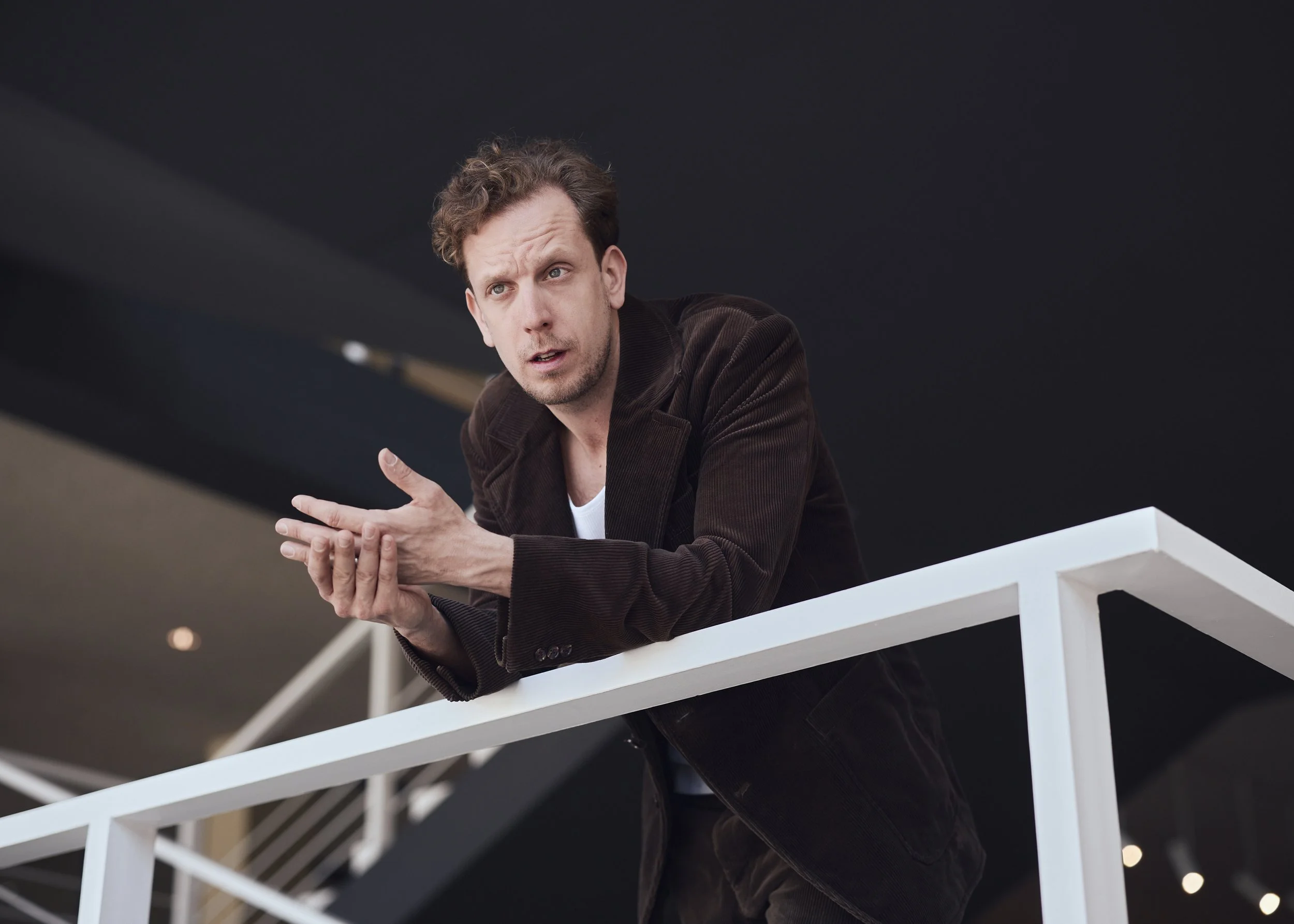 Schauspieler Henner Momann an Geländer, Hände reibend, in die Ferne schauend