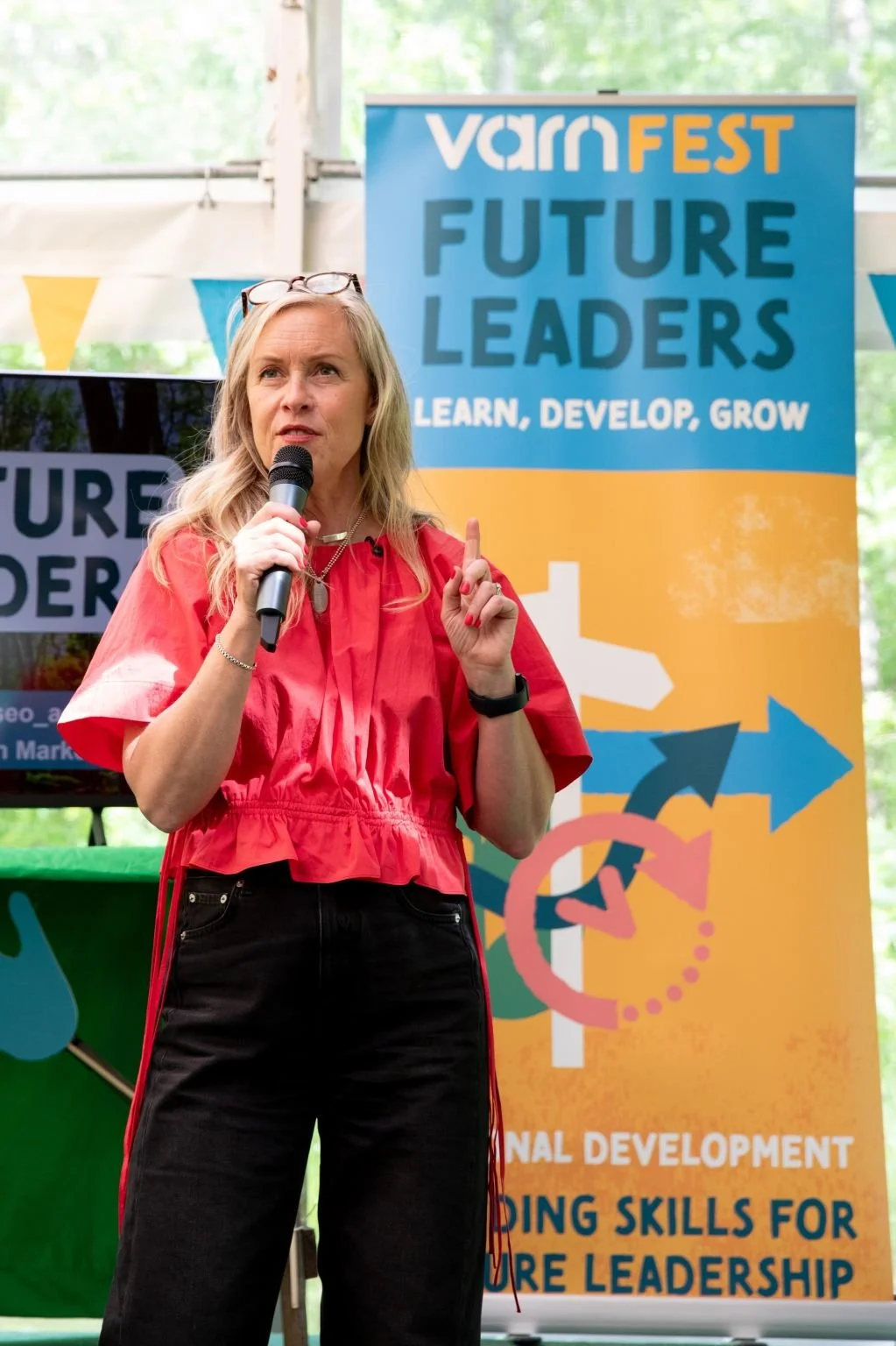 Fiona Craig speaking into a microphone at an event called 'VarnFEST' with a banner behind her that reads 'Future Leaders' and 'Learn, Develop, Grow'.