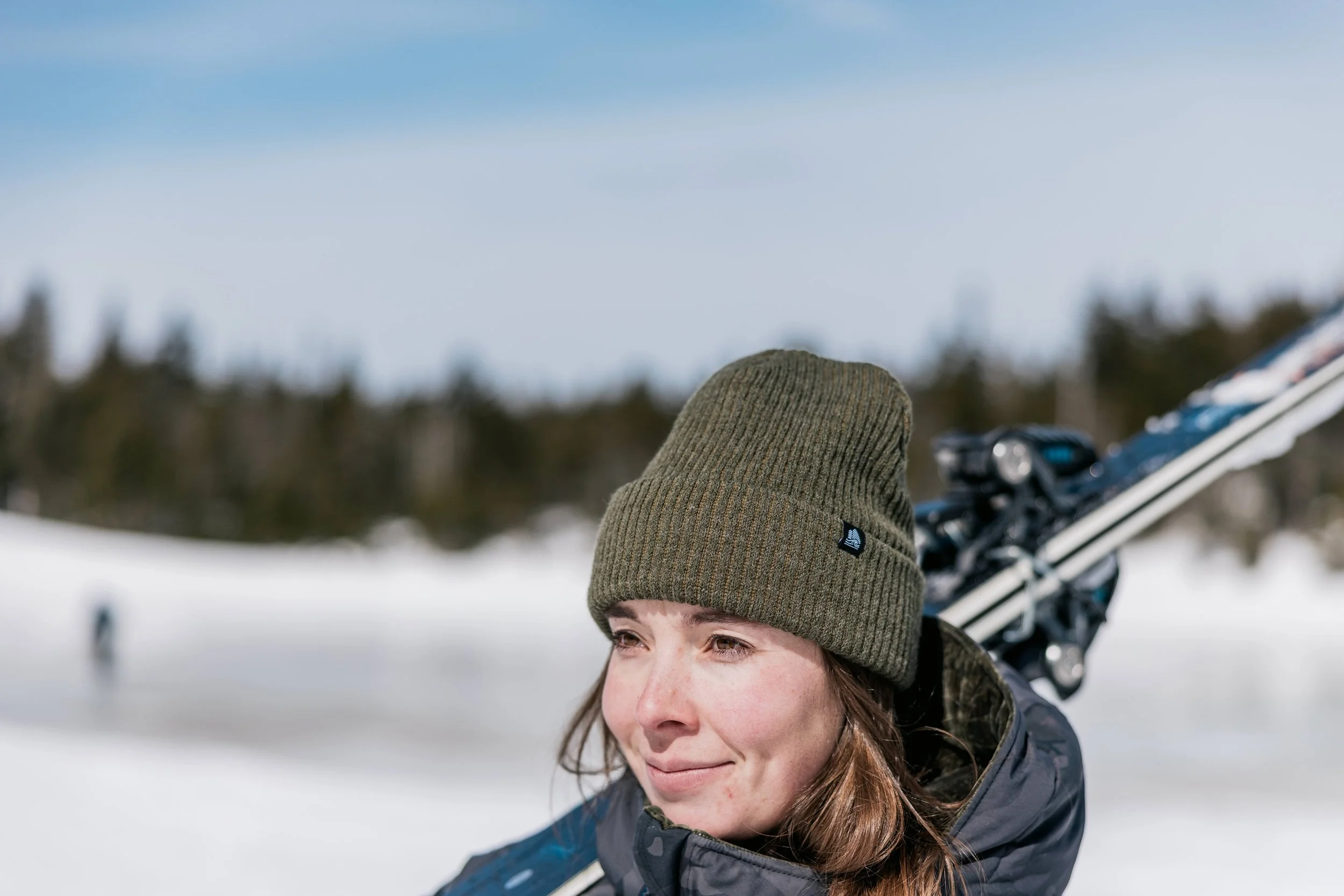 woman wearing a 4t2d beanie while carrying a pair of skis at stowe mountain