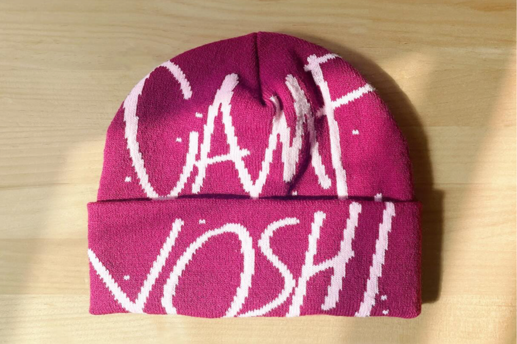 Pink knit beanie hat with white lettering that says 'CANT MISS' on a wooden surface.