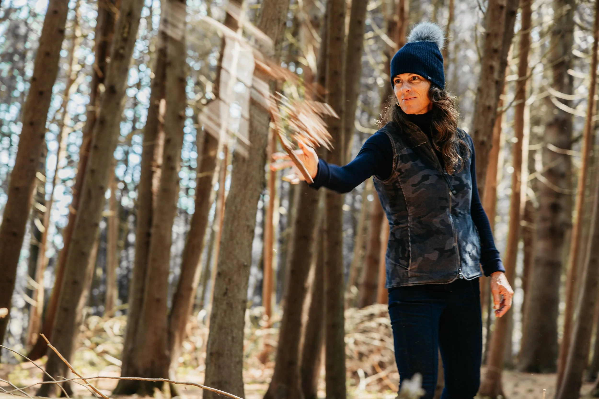 woman wearing a fourbital beanie throwing a stick in the woods