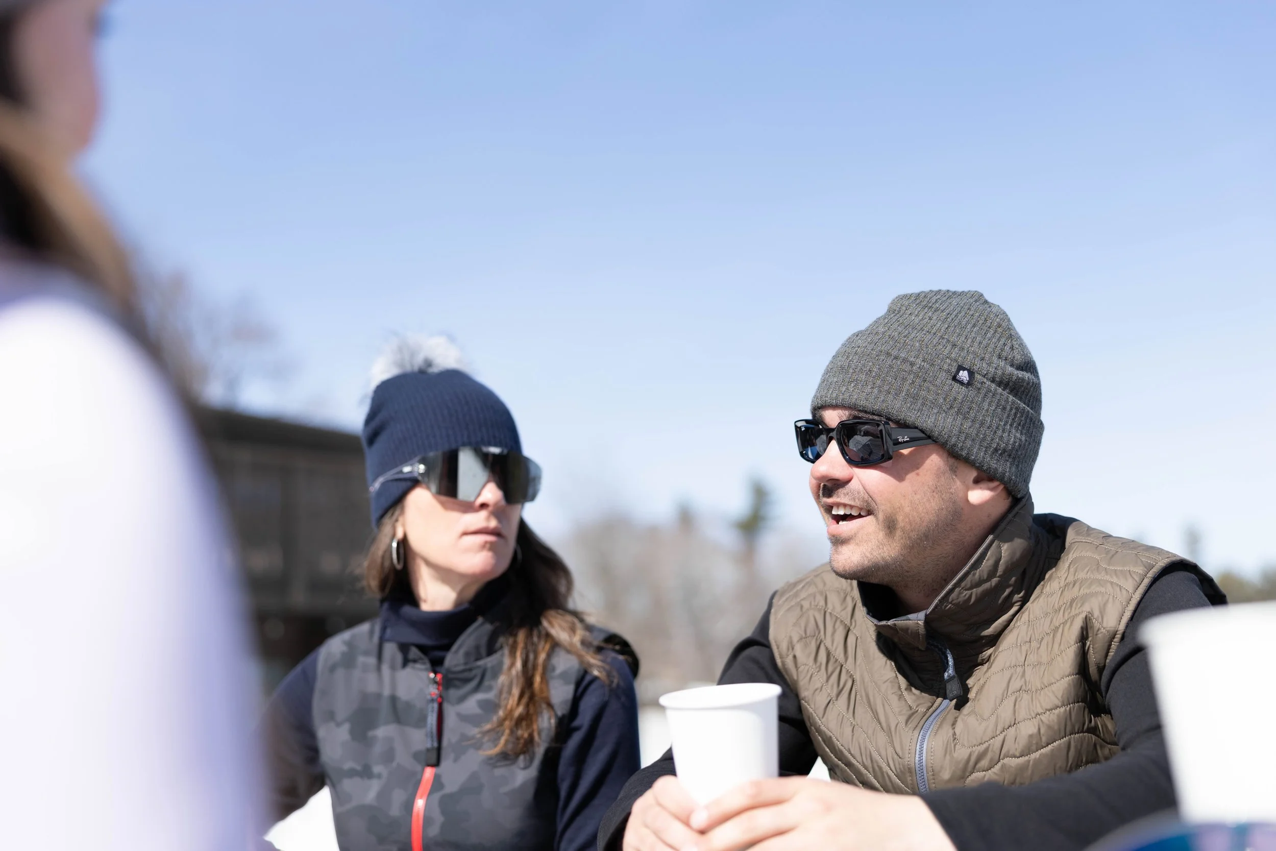 a woman and man outside on a cold sunny vermont day wearing beanies and sunglasses