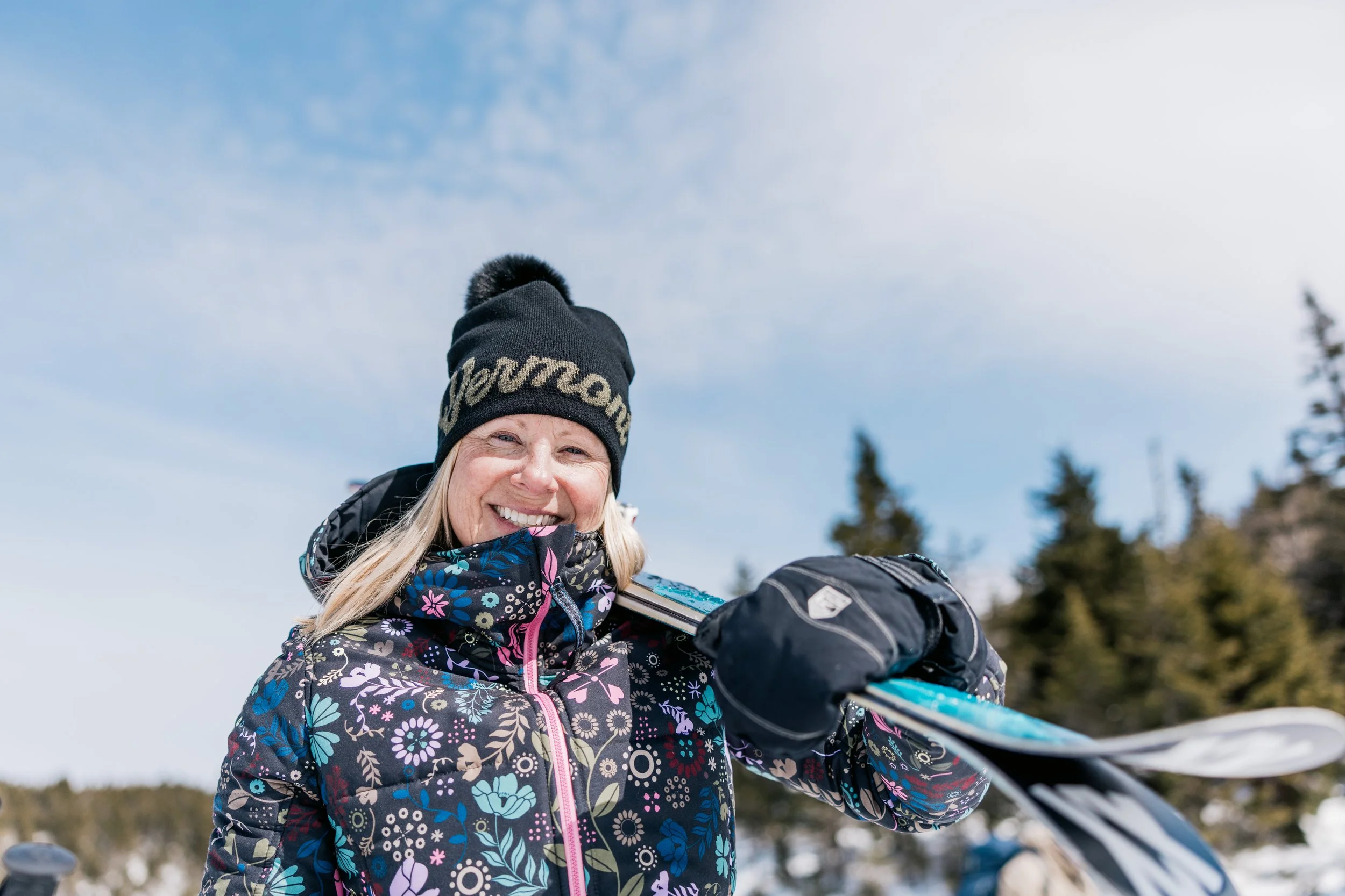 woman wearing a vermont beanie while carrying a pair of skis