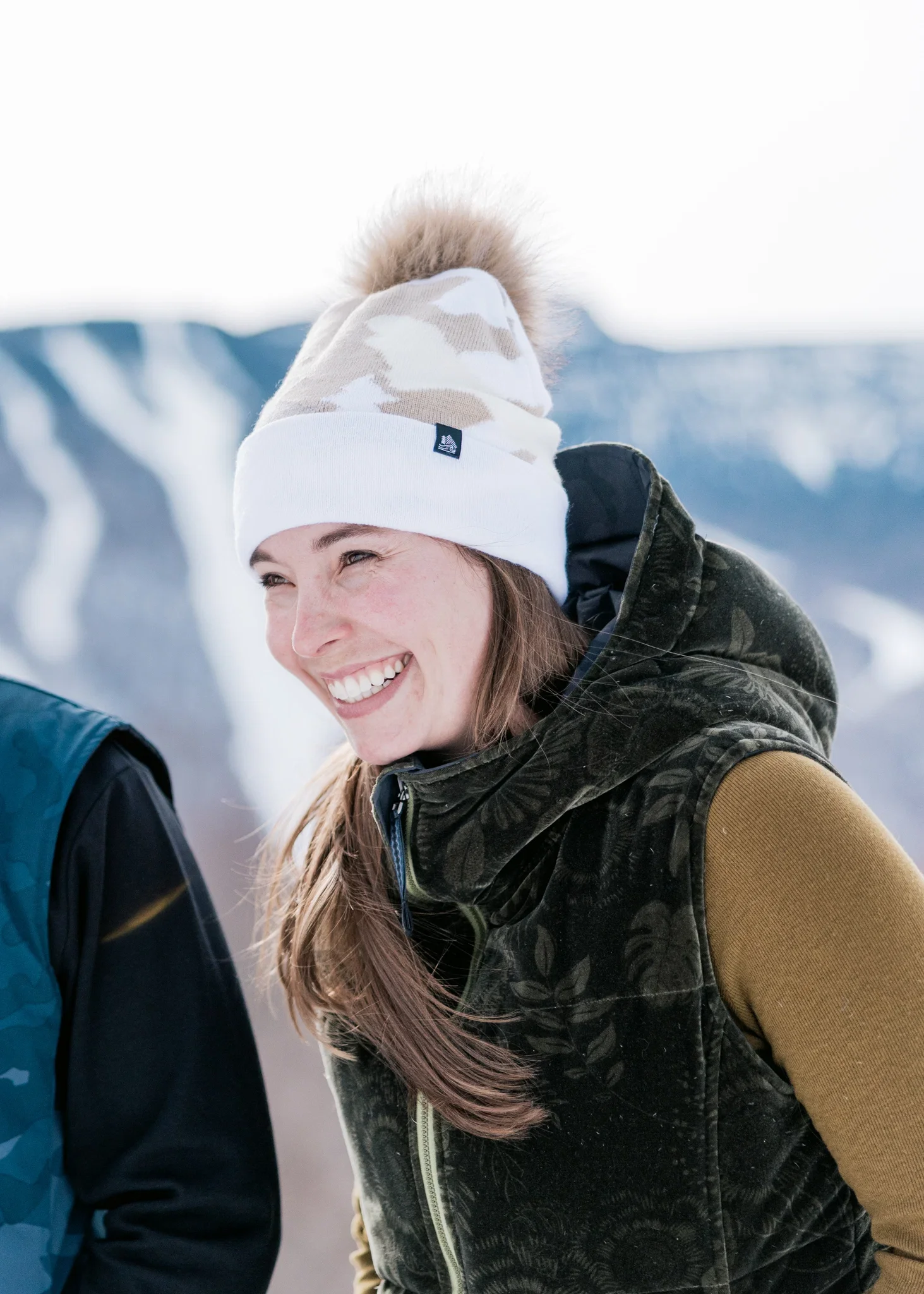 woman smiling and wearing a beanie made by fourbital factory in front of mount mansfield