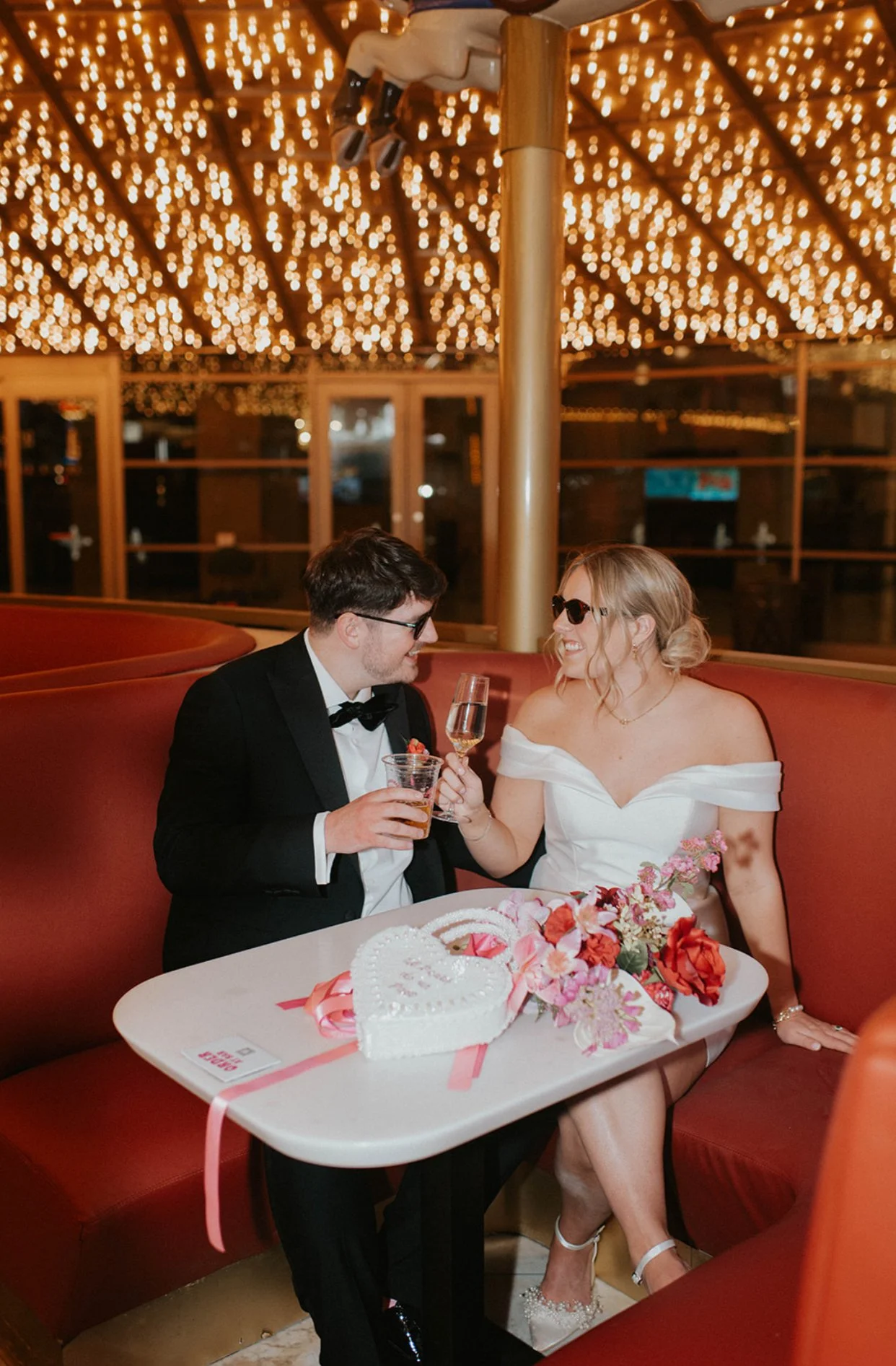 Betty and Joe celebrating with drinks beneath twinkling lights after their Las Vegas wedding ceremony at Sure Thing Chapel.