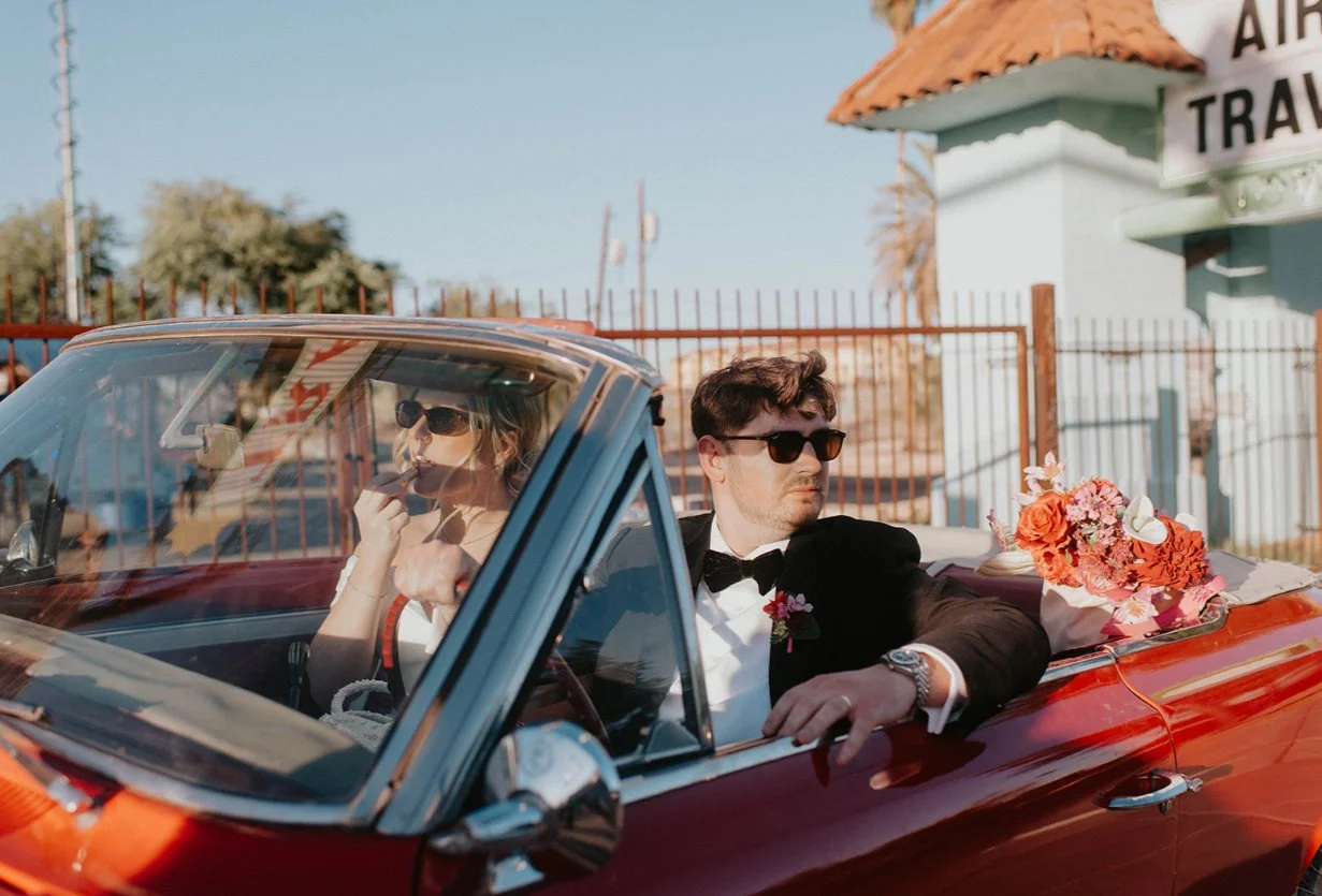 Betty and Joe sitting in a vintage red Mustang with their pink and red wedding flowers during their Las Vegas wedding photoshoot.