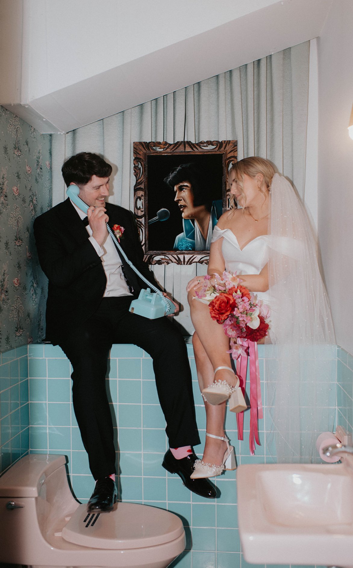 Betty and Joe posing with a retro telephone and vibrant wedding bouquet during their playful Las Vegas wedding portraits.