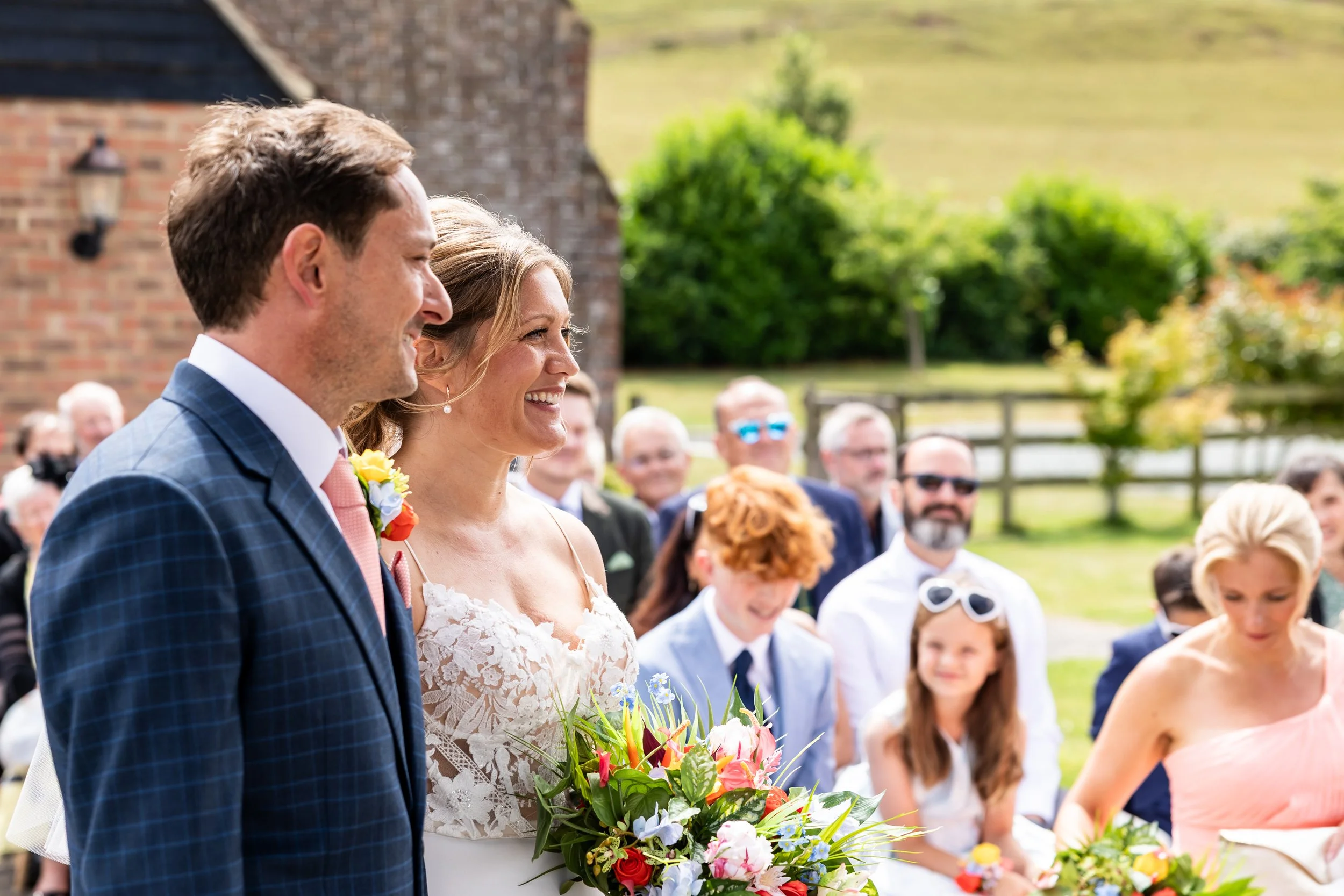 Anna and Christian with their wedding party at Long Furlong Barn featuring coral bridesmaid dresses, blue suits and colourful silk wedding flowers.