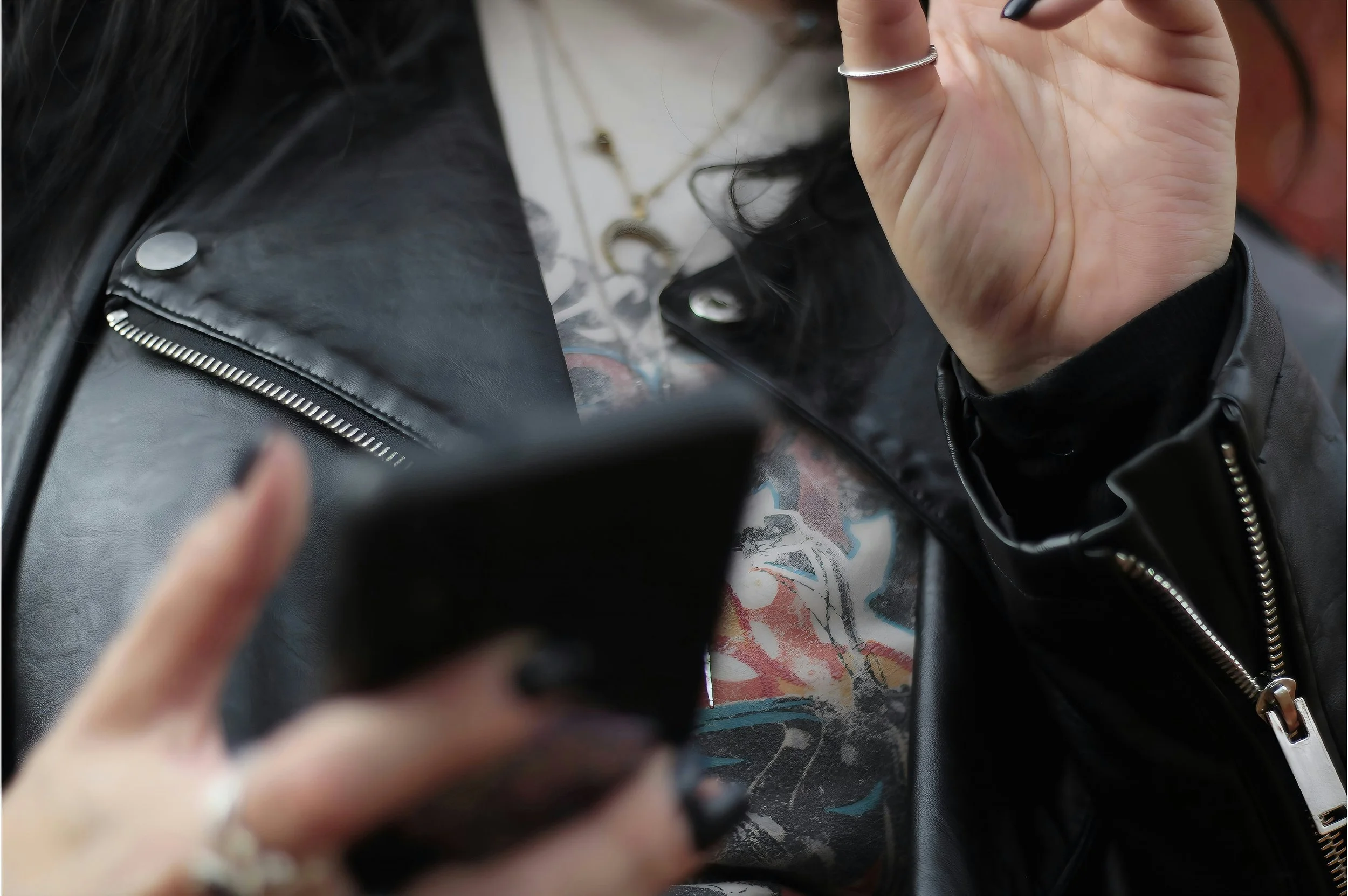 woman in a black leather jacket with black nails using a black cellphone
