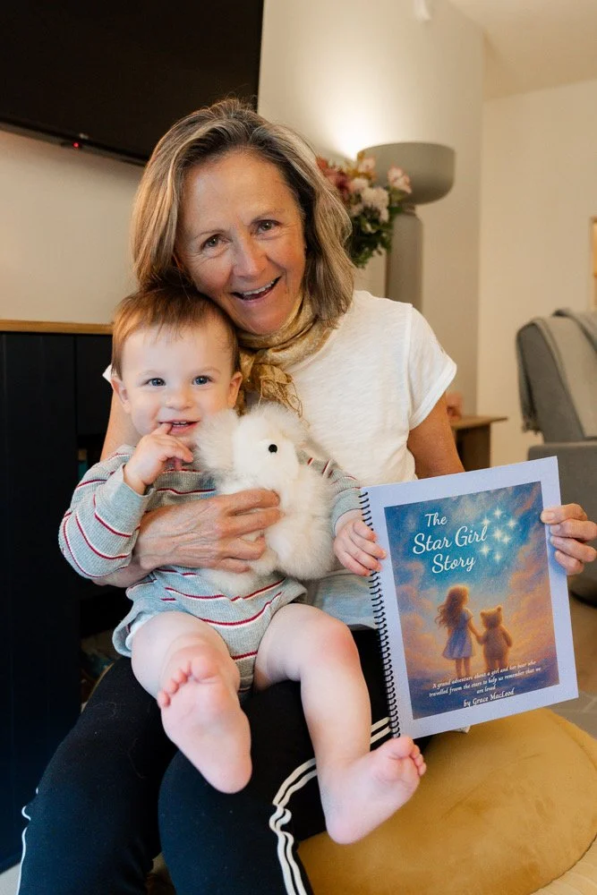A woman and a young child smiling together on a couch, holding a fluffy white toy and a book titled 'The Star Girl Story' with a cover illustration of a girl and a teddy bear watching the stars.