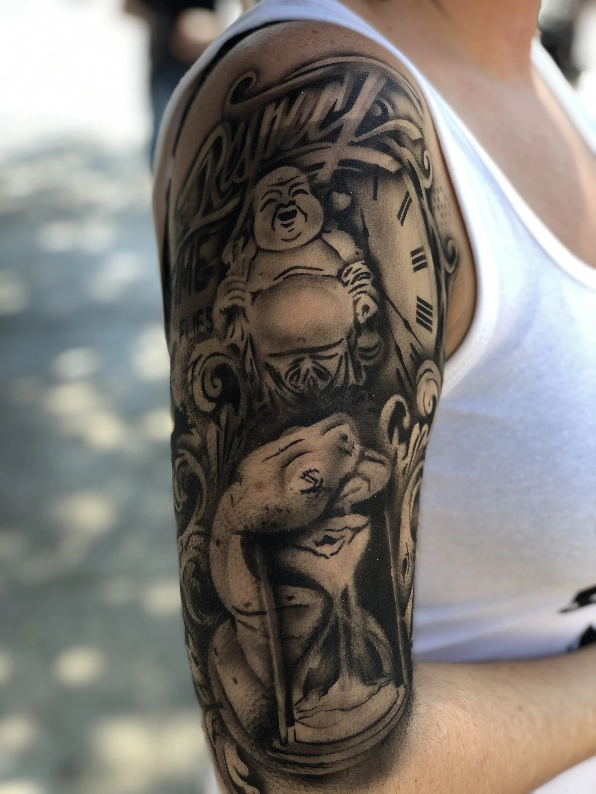 Arm tattoo featuring Buddha, clock, and snake themes in black and gray ink.