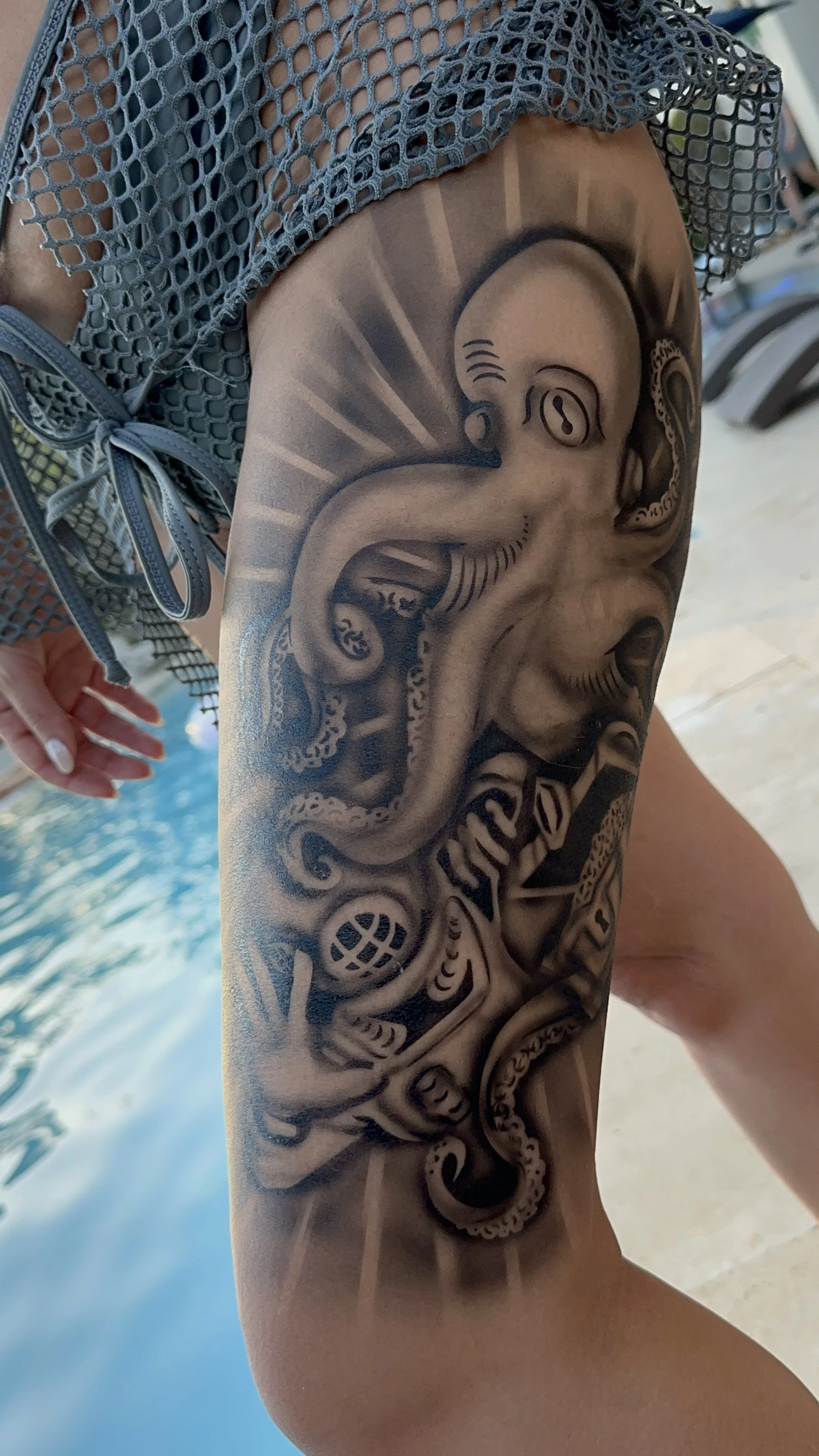 Black and gray octopus tattoo on a person's thigh next to a pool.