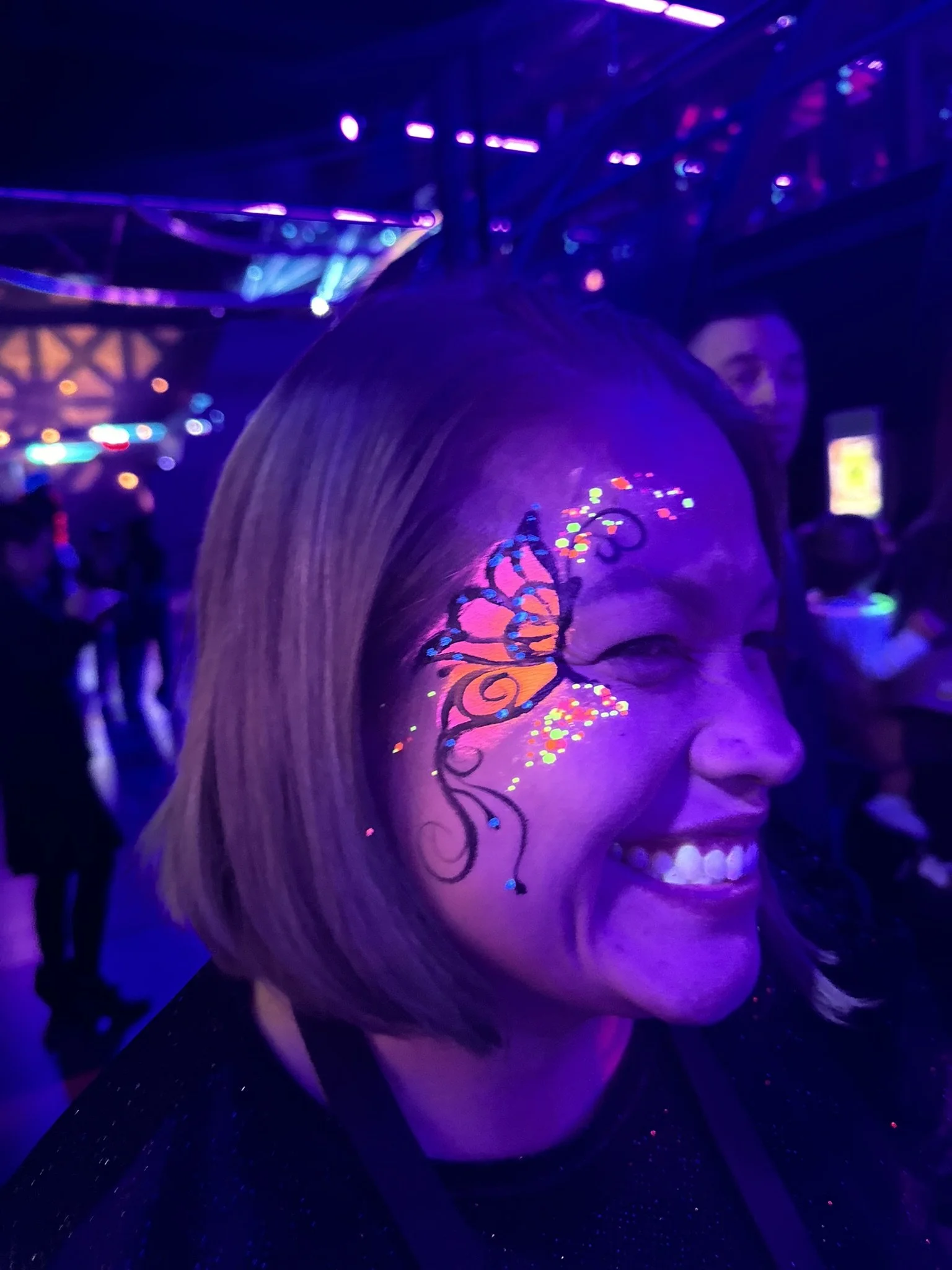 Person with glowing face paint art in a dark, neon-lit environment.
