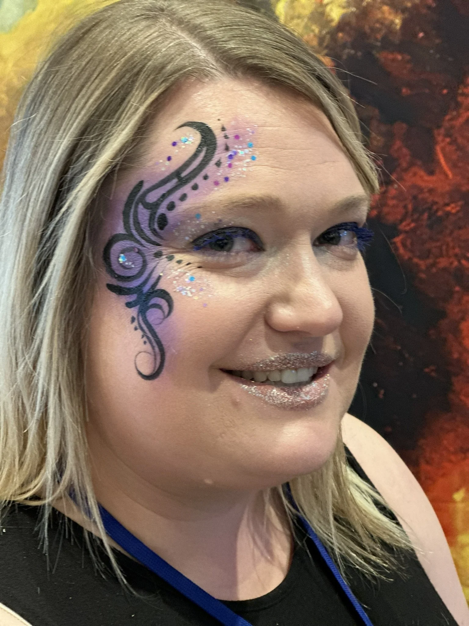 Person with creative face paint and glitter lipstick smiling