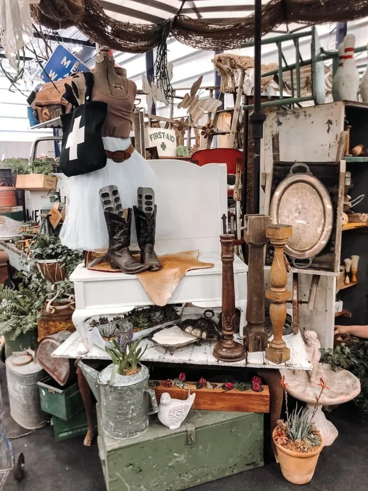 A display of vintage and rustic goods, including wooden candlestick holders, rustic tables, and some clothing.