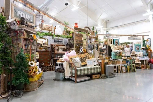 Vintage market with a green and white plaid daybed covered in throw pillows, surrounded by vintage tables, and shelves of other decorative items. 