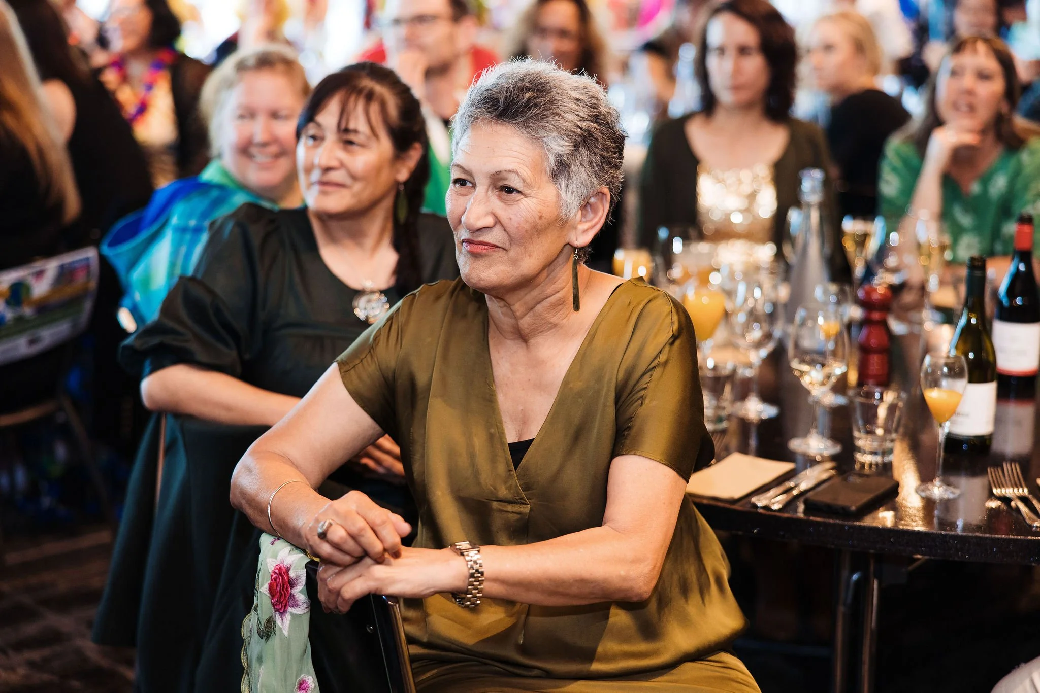 Guests connecting at the Combined Community Trusts Conference gala dinner. A diverse group of women seated at a banquet table during a social event or celebration, smiling and engaging. Bottles and glasses are on the table.