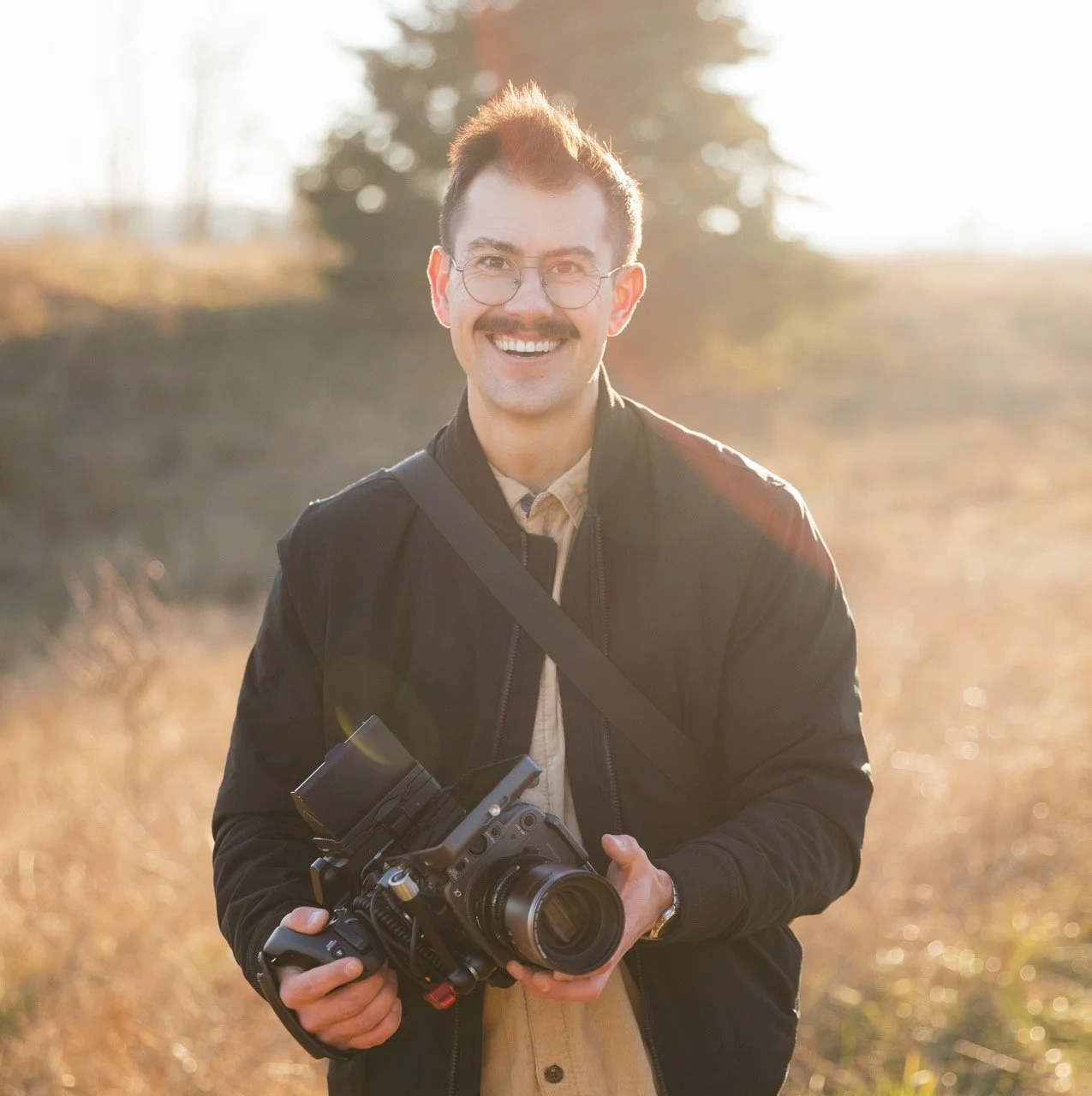 Cody McDonald smiling in a golden field with a cinema camera in his hands