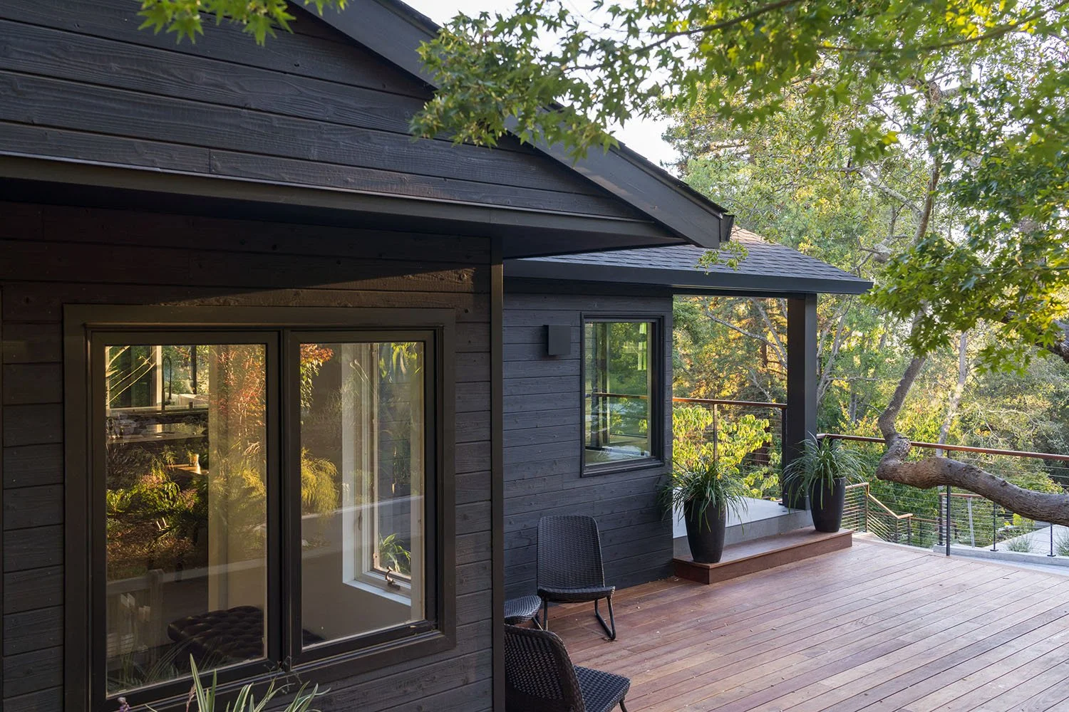 Dark wood-clad exterior and deck of the Orinda house renovation by Tierney Conner, set within mature East Bay oak trees.