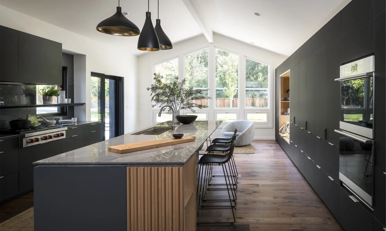Sunset Magazine feature spread showcasing a modern black kitchen with a waterfall island, wood slat base, cathedral ceiling, and garden-facing windows.