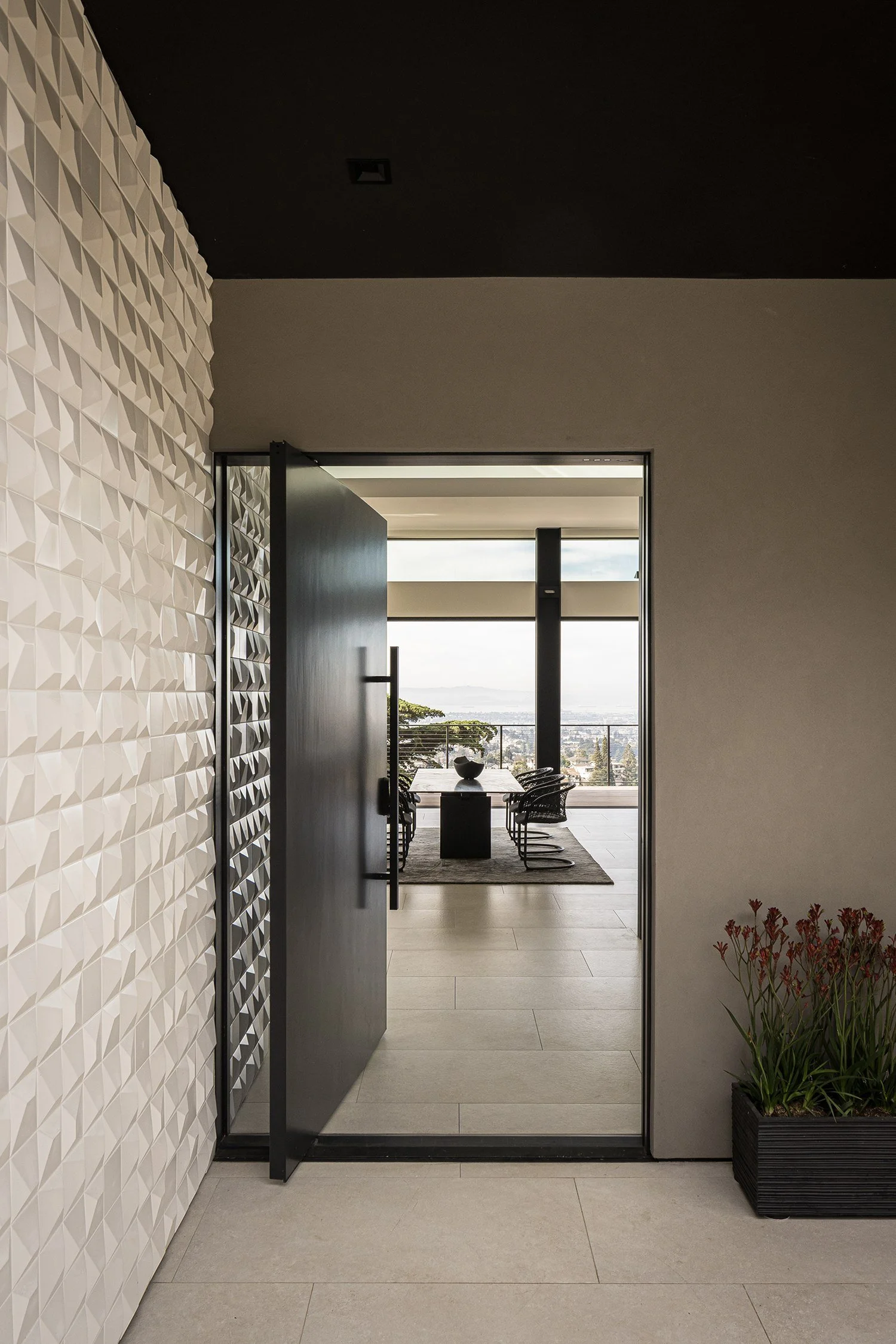 Black pivot entry door framed by 3D white tile wall in a modern hillside residence by Tierney Conner Architecture.