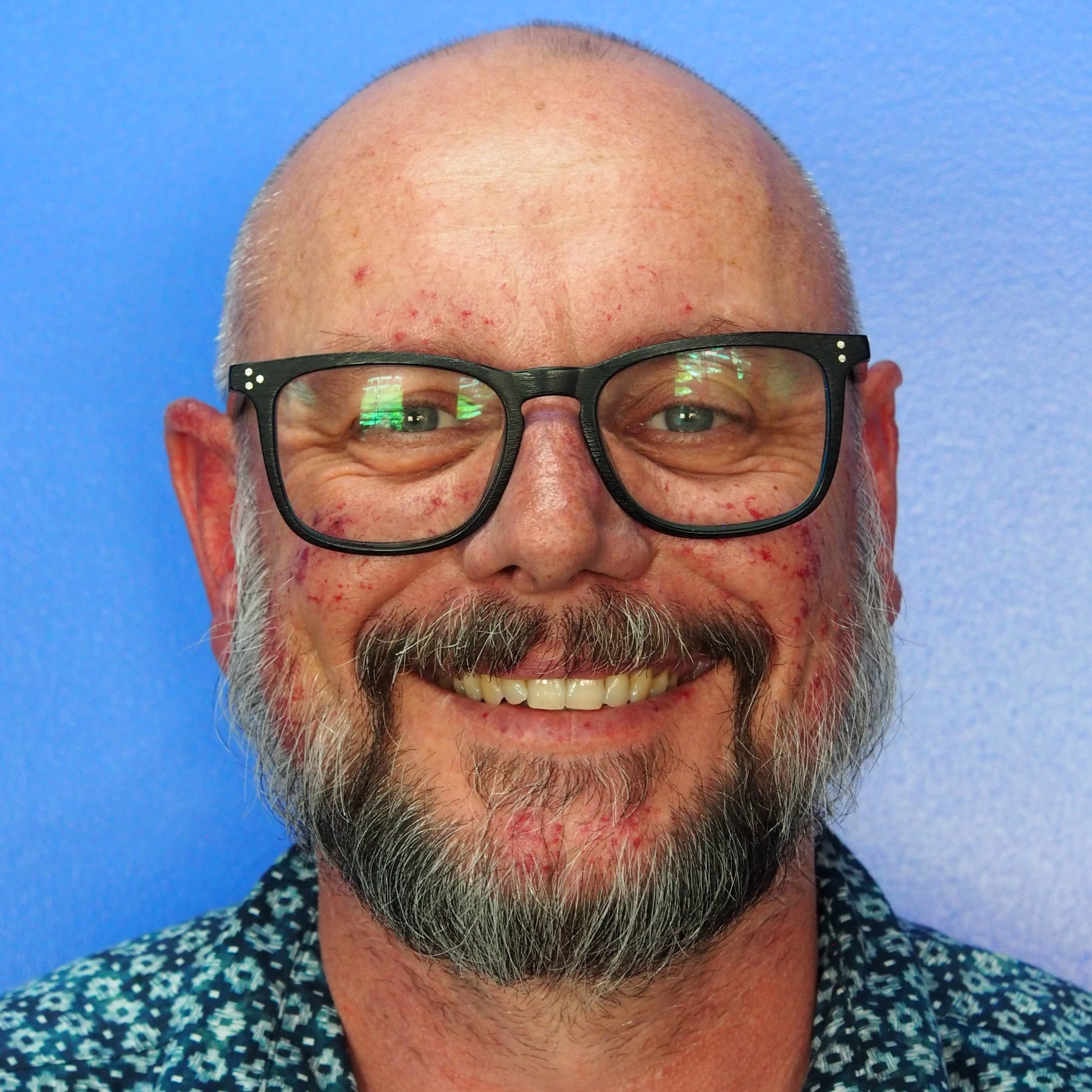 A man wearing a patterned top against a blue background.