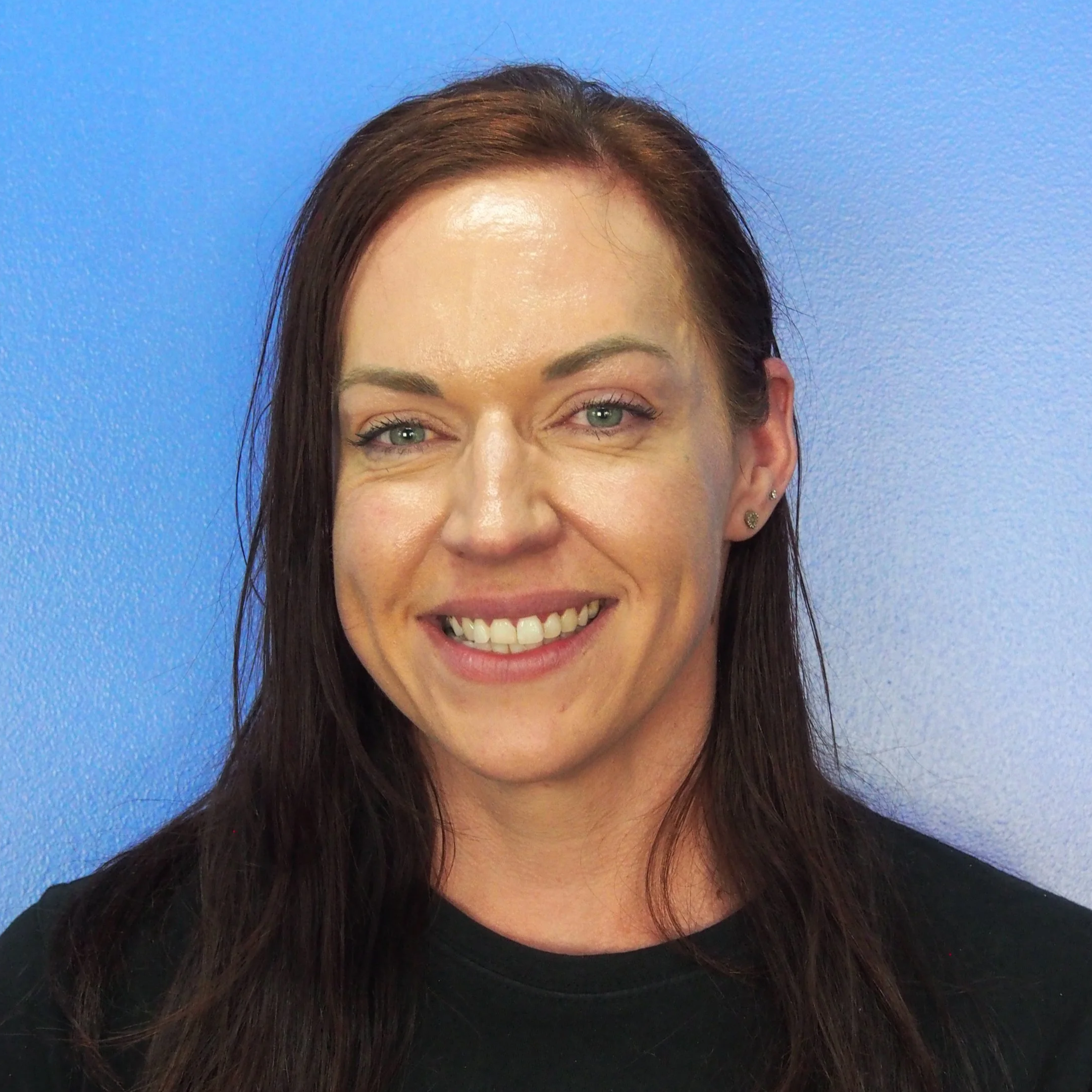 A woman with dark hair wearing black shirt standing against blue wall.