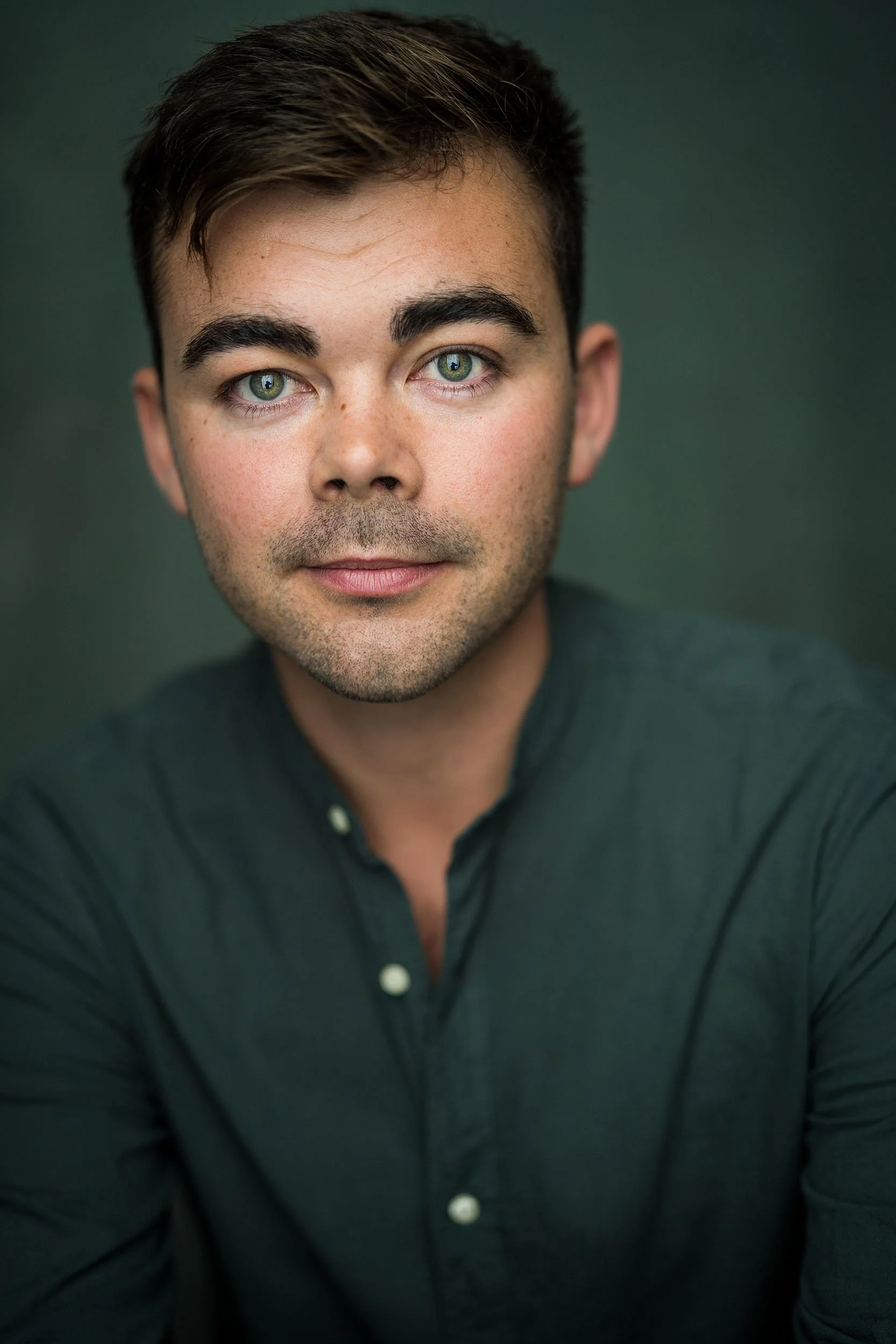 Portrait headshot of Andrew McNicol wearing a dark green shirt against a soft green background.