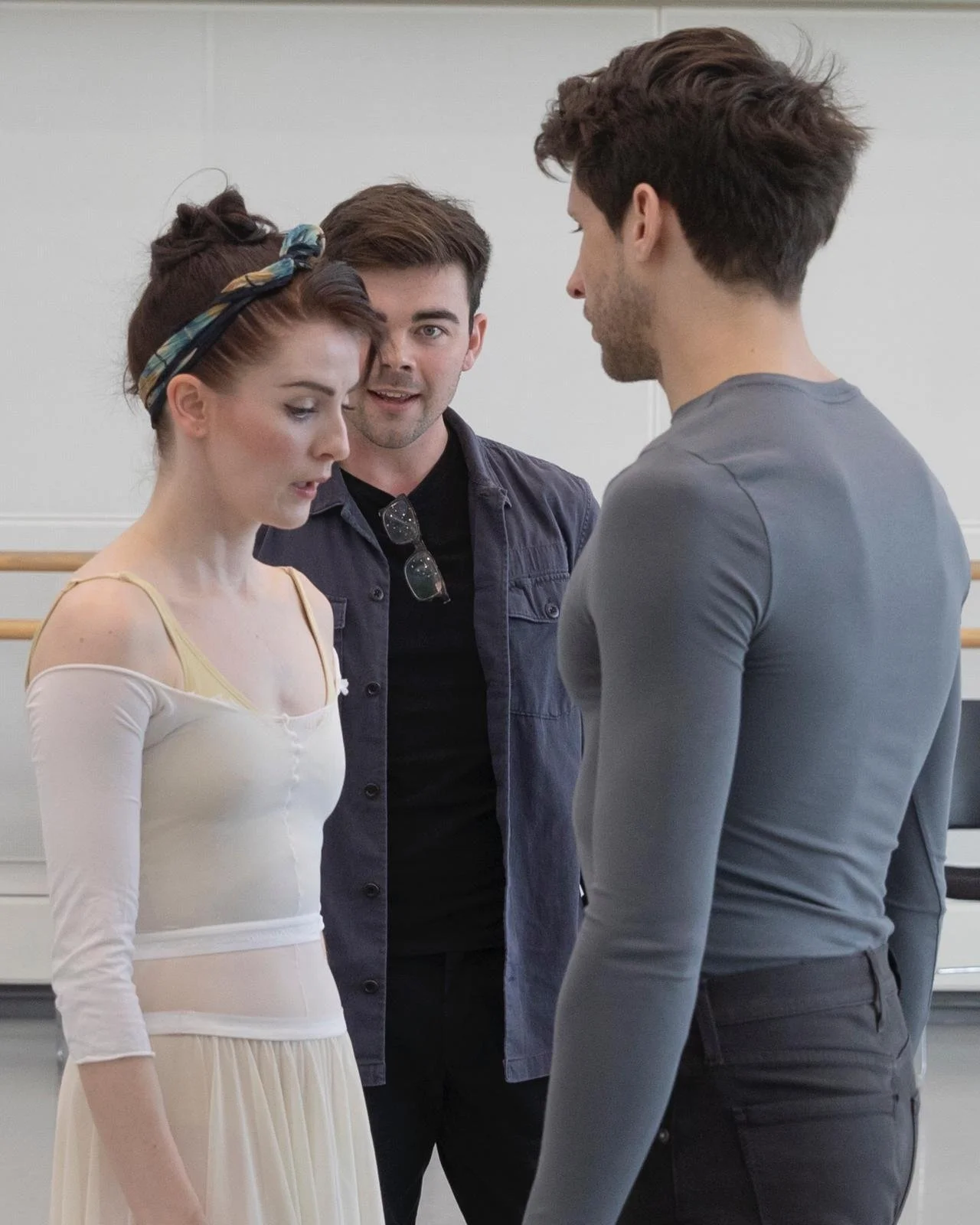 Andrew McNicol speaks with two dancers during a rehearsal in a studio, standing between them as they prepare a scene.
