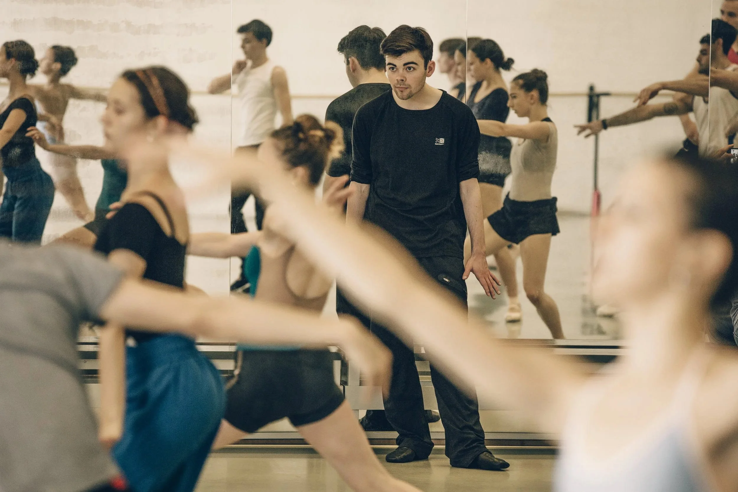 Andrew McNicol leads dancers during a Choreolab rehearsal in a studio, with dancers moving in the foreground.