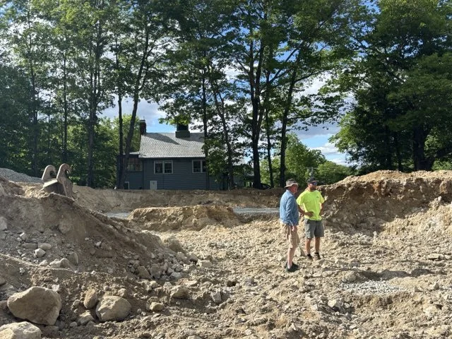 Two men stand in a hole dug where a house's foundation should be