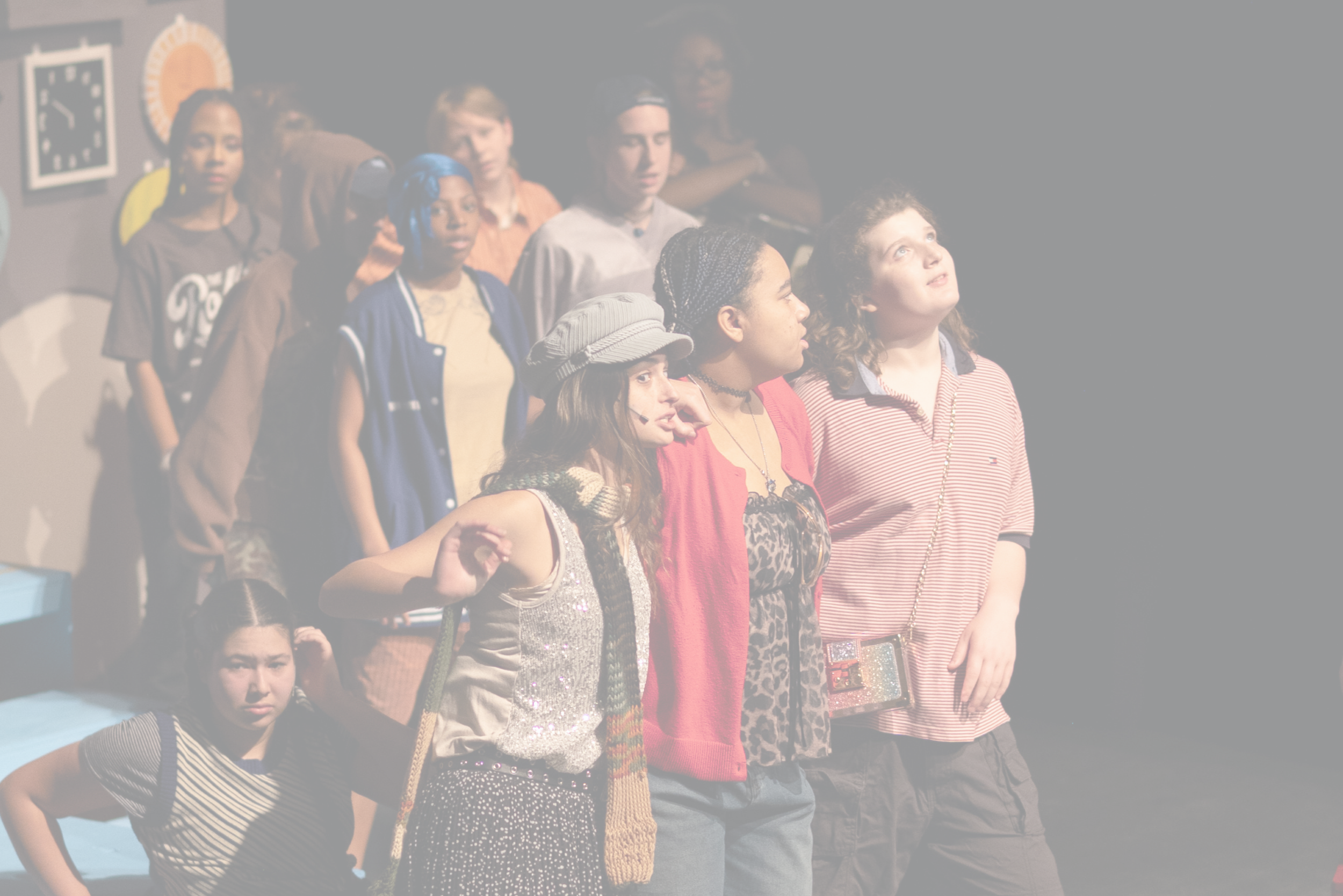 A group of children on stage performing in a play, with some children pointing upward and smiling, one child in the foreground with curly hair raising their hand. | Yes! And Collaborative Arts
