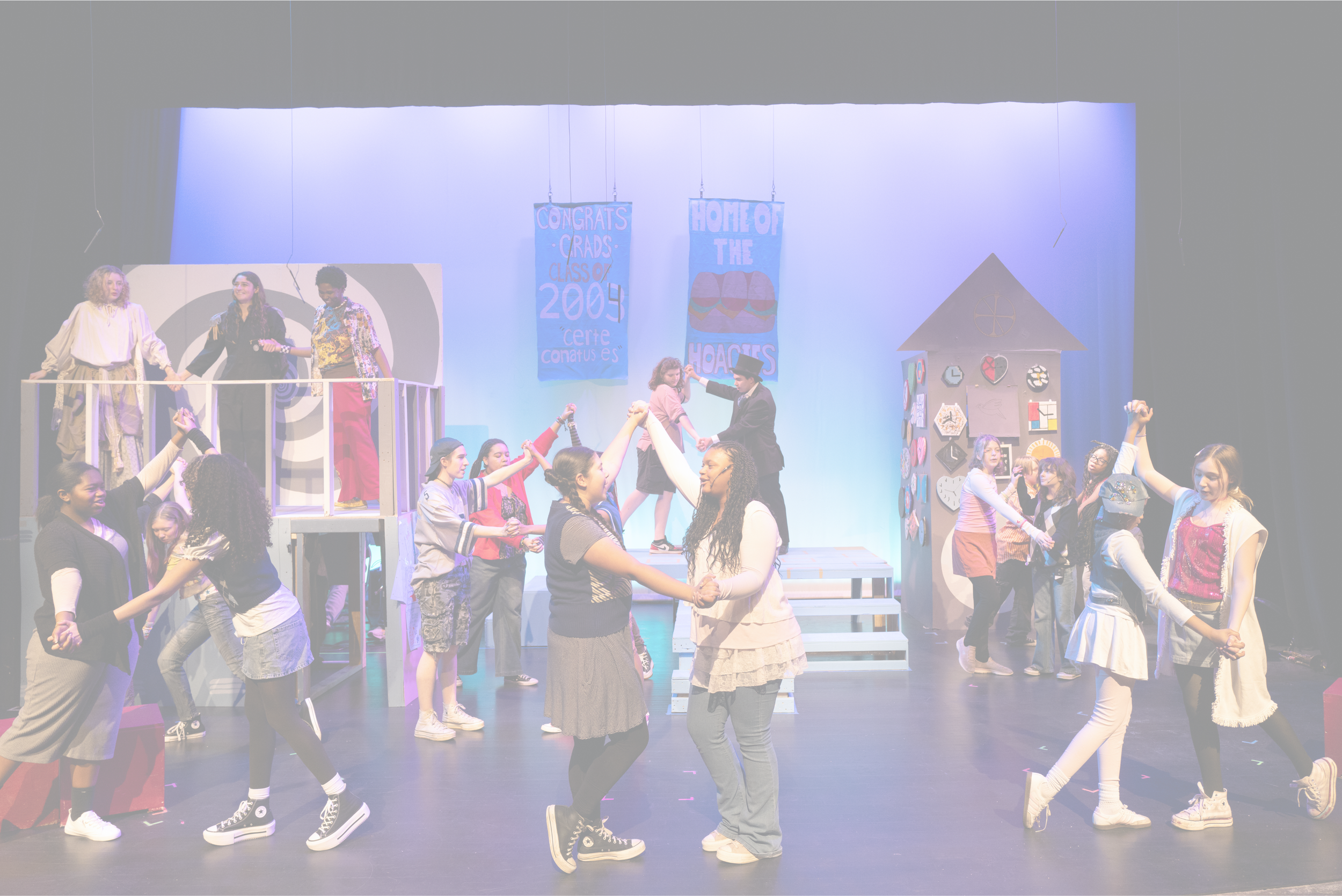 A group of children and teenagers on stage, performing with expressive faces and gestures, in front of a blue background with stage props. | Yes! And Collaborative Arts