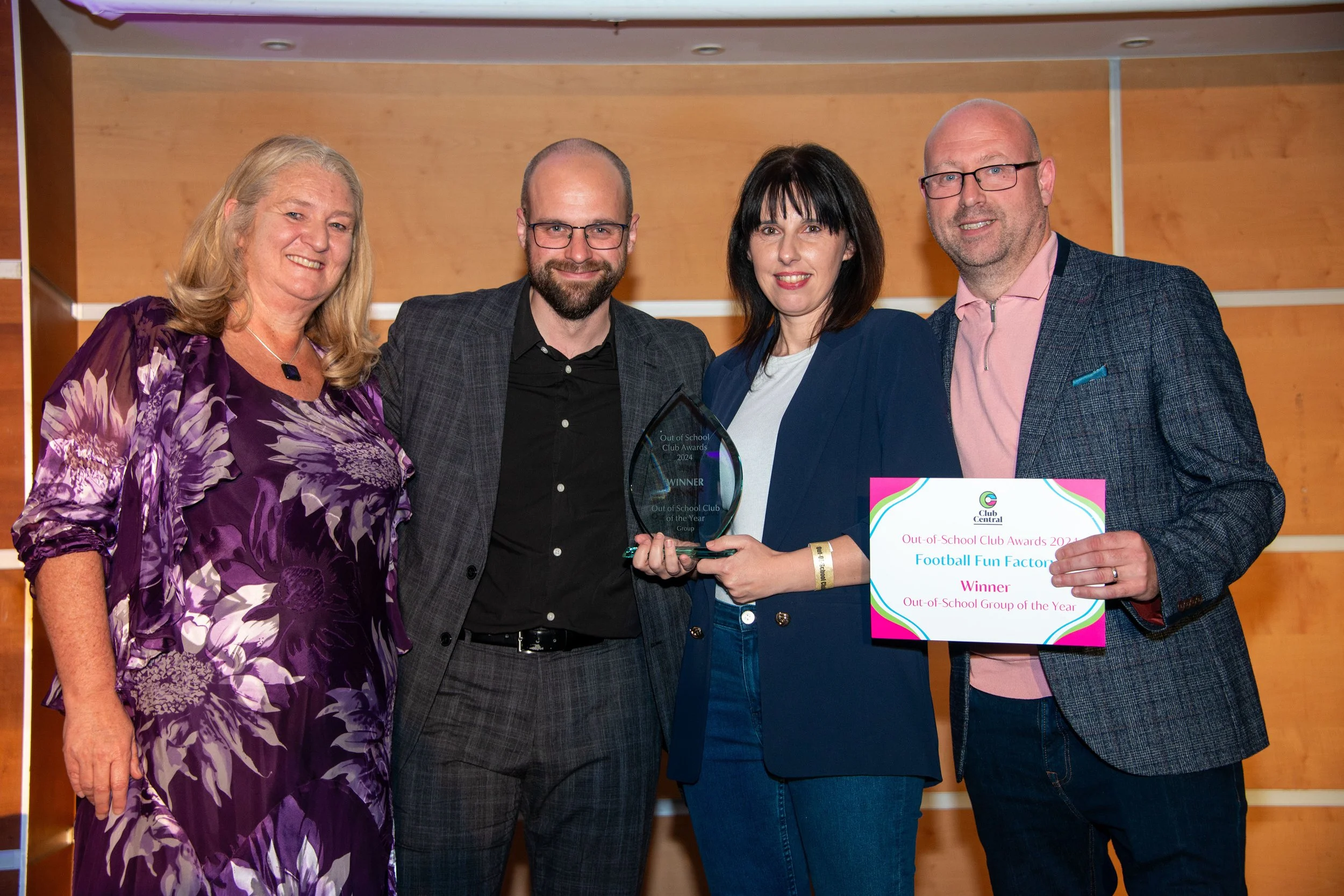 Photo of 4 smiling people.  One holding a certificate, one holding a glass award and a male and female also smiling at the camera