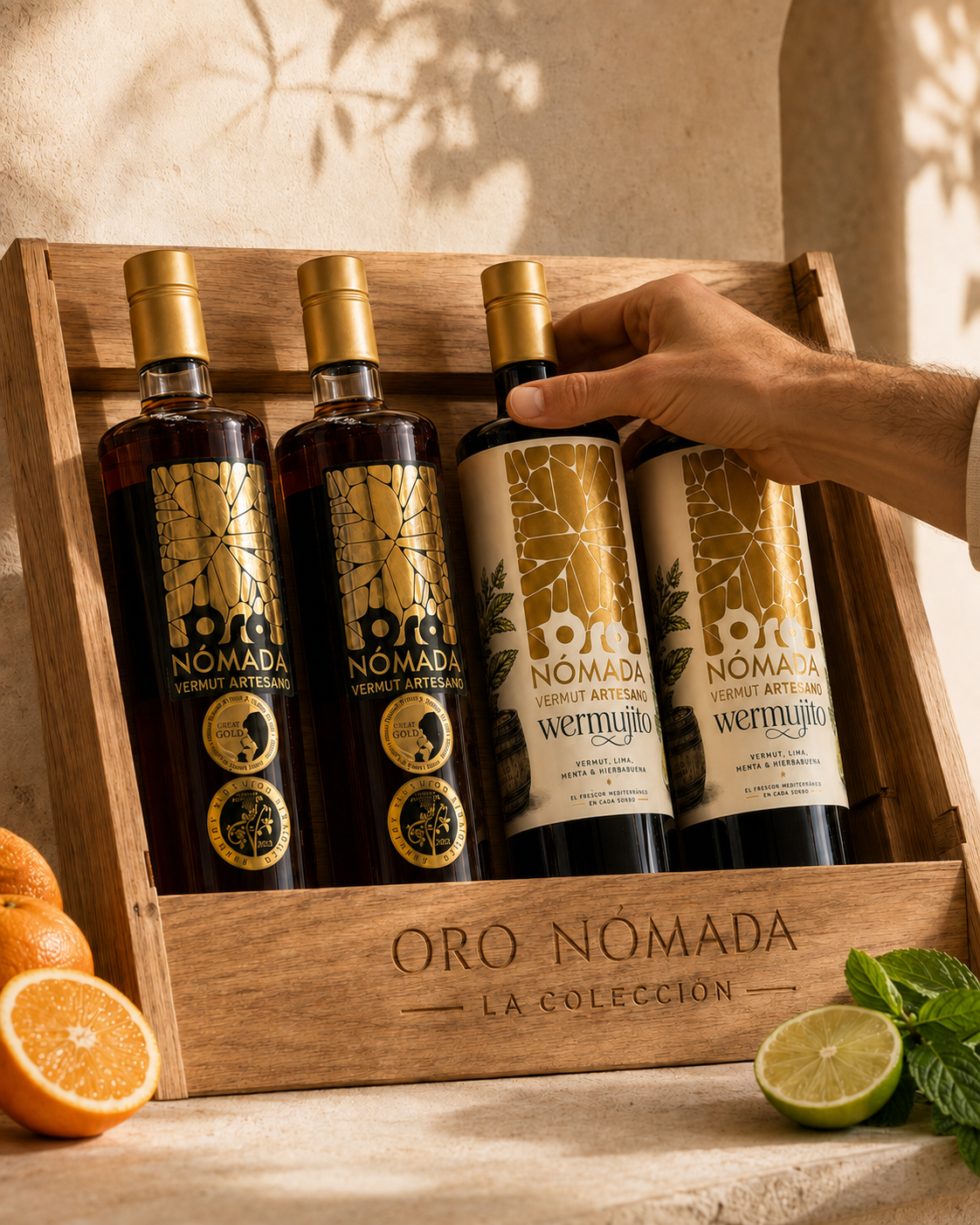 Cuatro botellas de Oro Nómada Vermut Artesano en una bandeja de madera con etiquetas doradas y negras, una de ellas sostenida por una mano. Frutas cítricas y hojas de menta decoran el fondo.