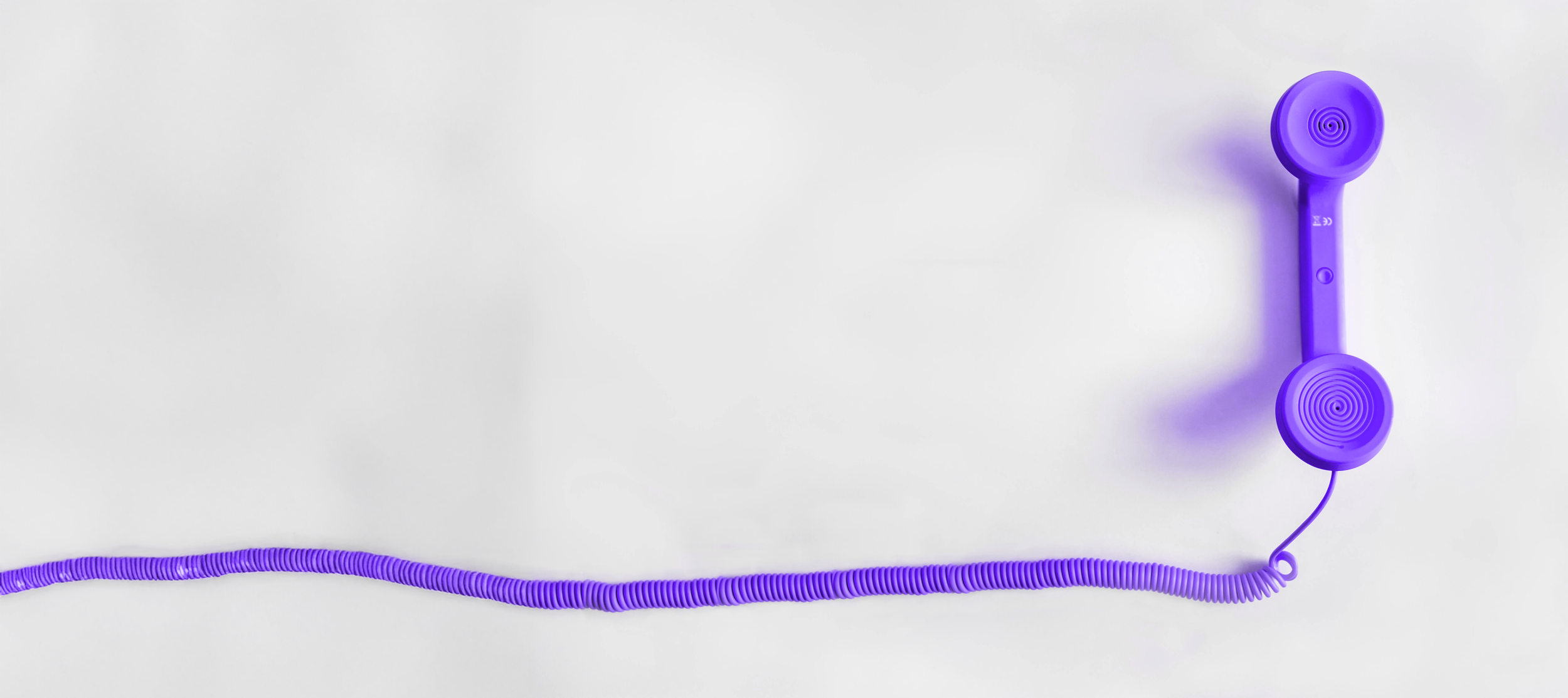 A wired purple hand held phone with its cord disappearing offscreen.