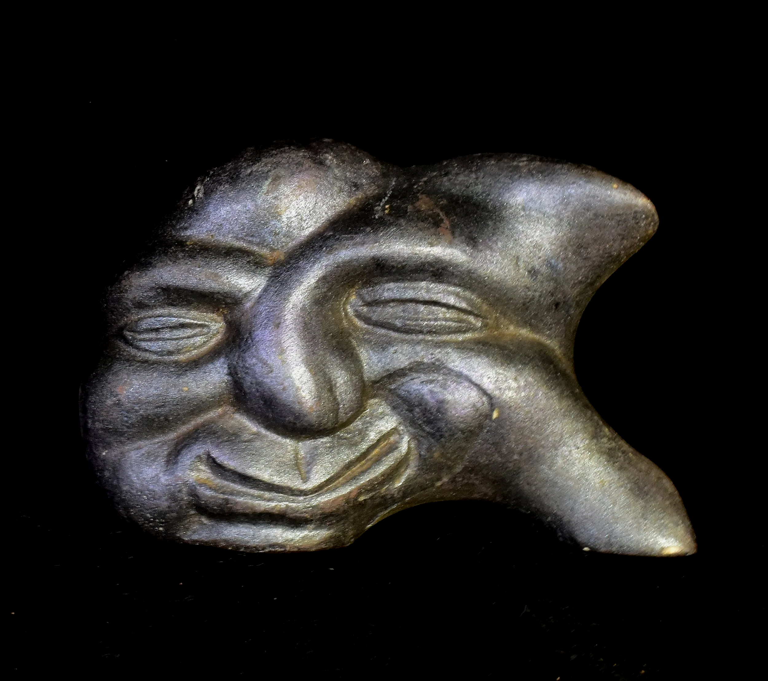 Close-up of a carved stone face against a black background, showing detailed features and expression.