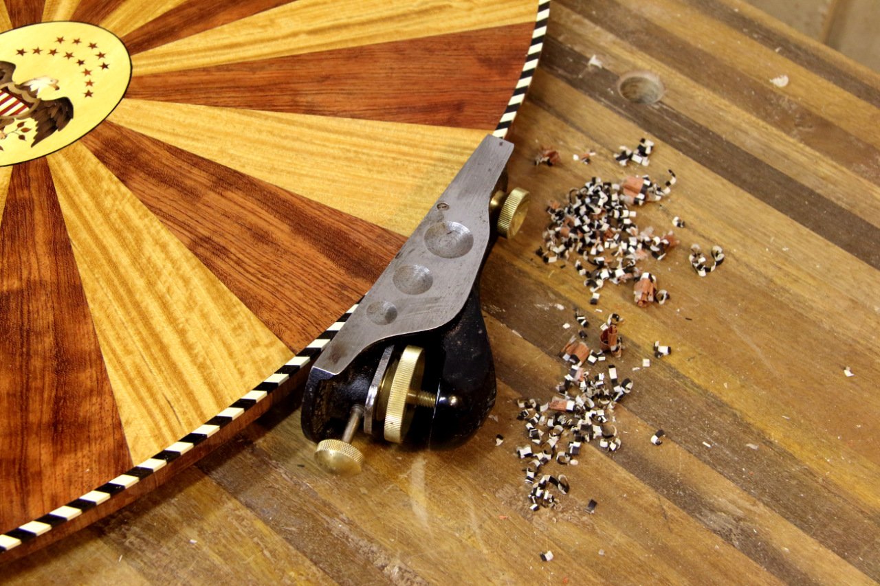 Hand planing the edge of a reproduction Salem Boston tilt top tea table with a marquetry inlay of an American Eagle and radial bands of Mahogany and Satinwood.