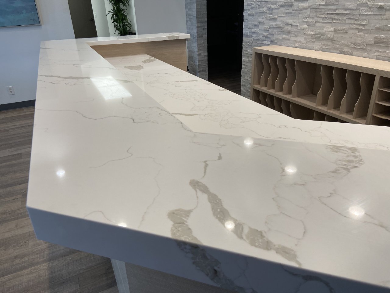 Modern reception desk with a glossy finish stone counter top and wooden shelving units in a bright office space.