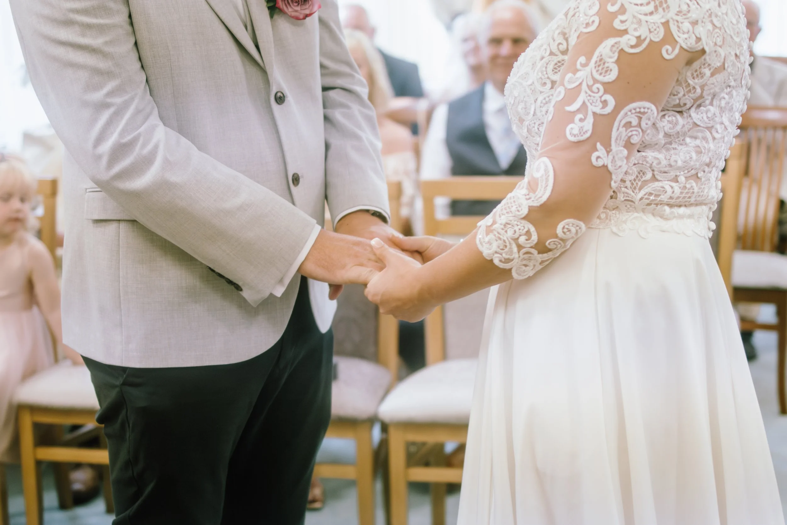 A couple holding hands during a wedding ceremony, with guests seated in the background. Swansea Registry Office.