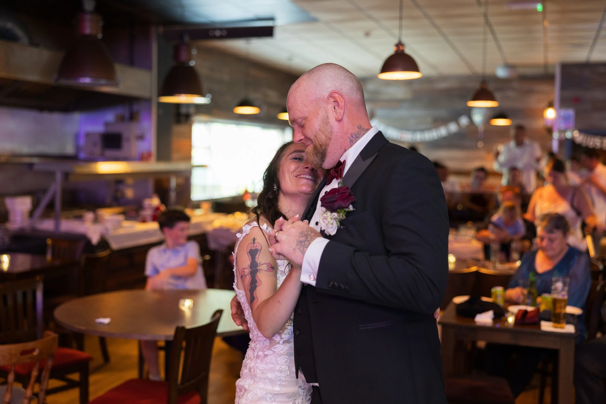 A bride and groom share a dance at their wedding reception, surrounded by seated guests in a decorated indoor venue.