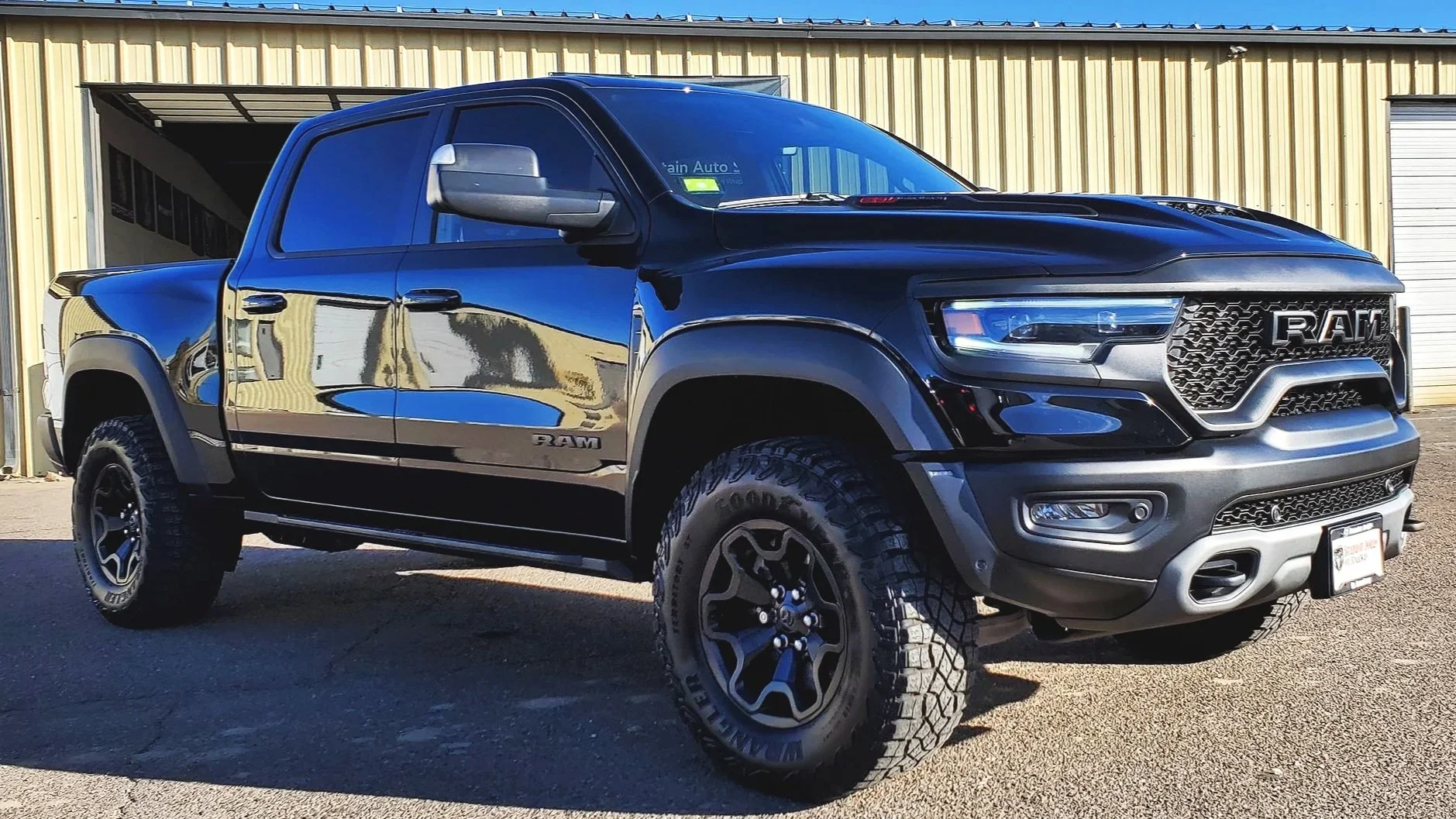 Black Ram TRX pickup truck parked outside a yellow metal building on a sunny day.