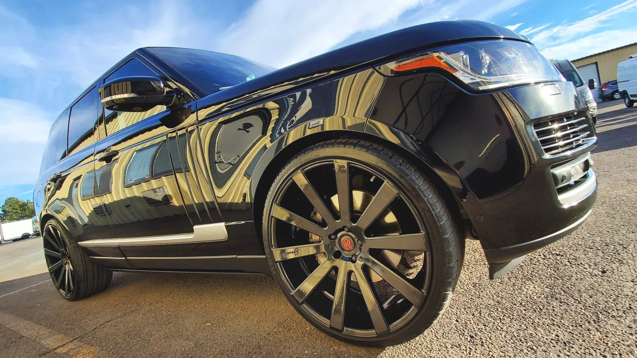 Black luxury SUV parked in an outdoor lot, reflecting striped buildings on its glossy surface, with large black wheels and a distinctive Rolls-Royce logo