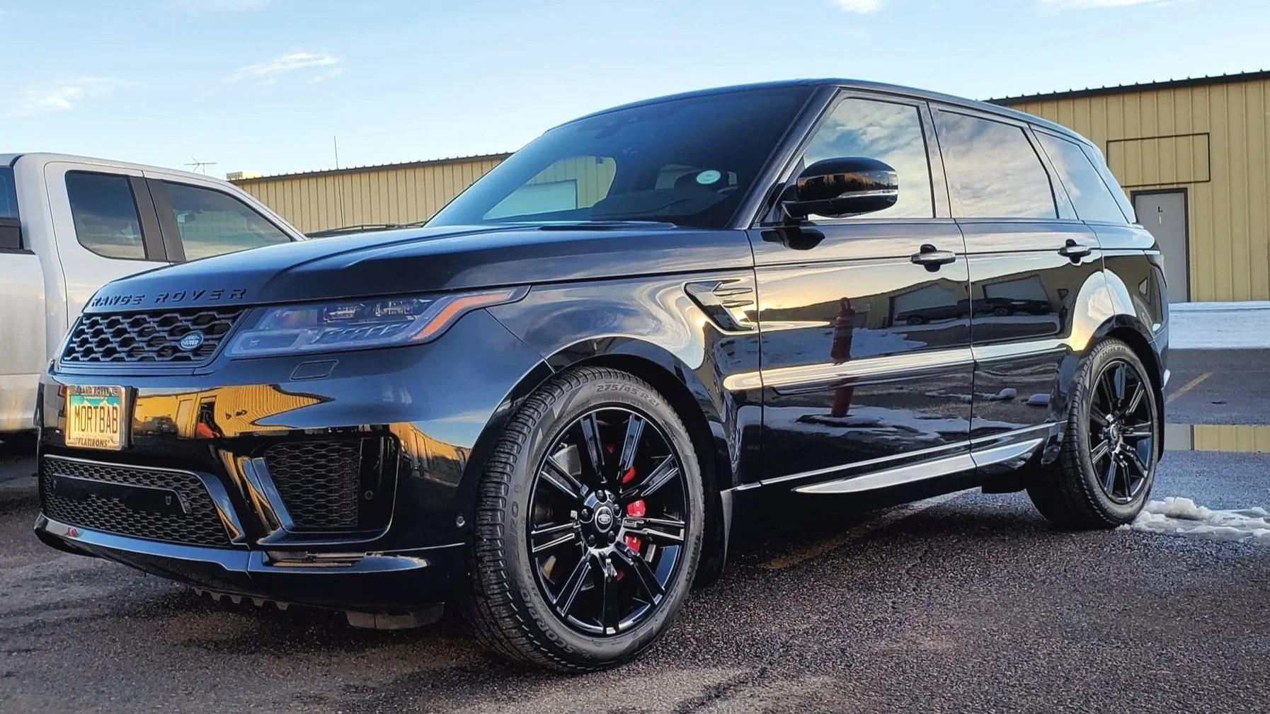 Black Range Rover SUV parked in a lot with a yellow building in the background and snow on the ground.