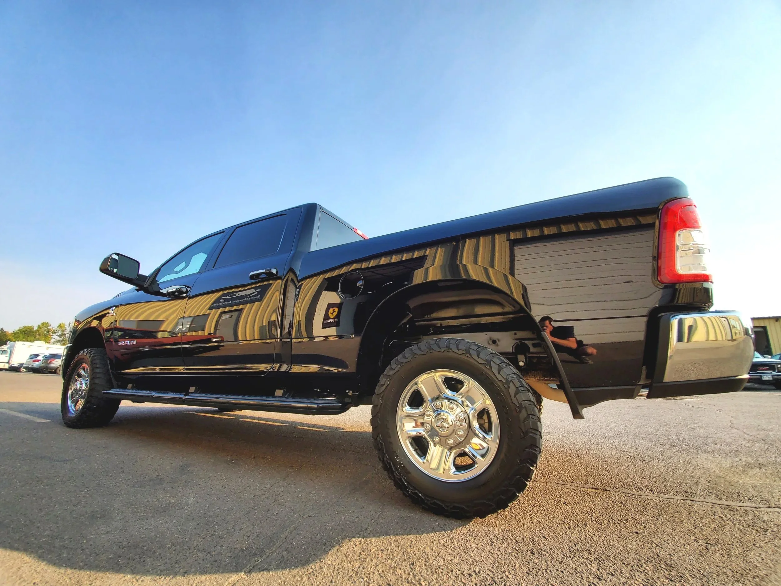Black pickup truck parked on a lot, reflected building in the background, and a person crouching near the truck's rear wheel