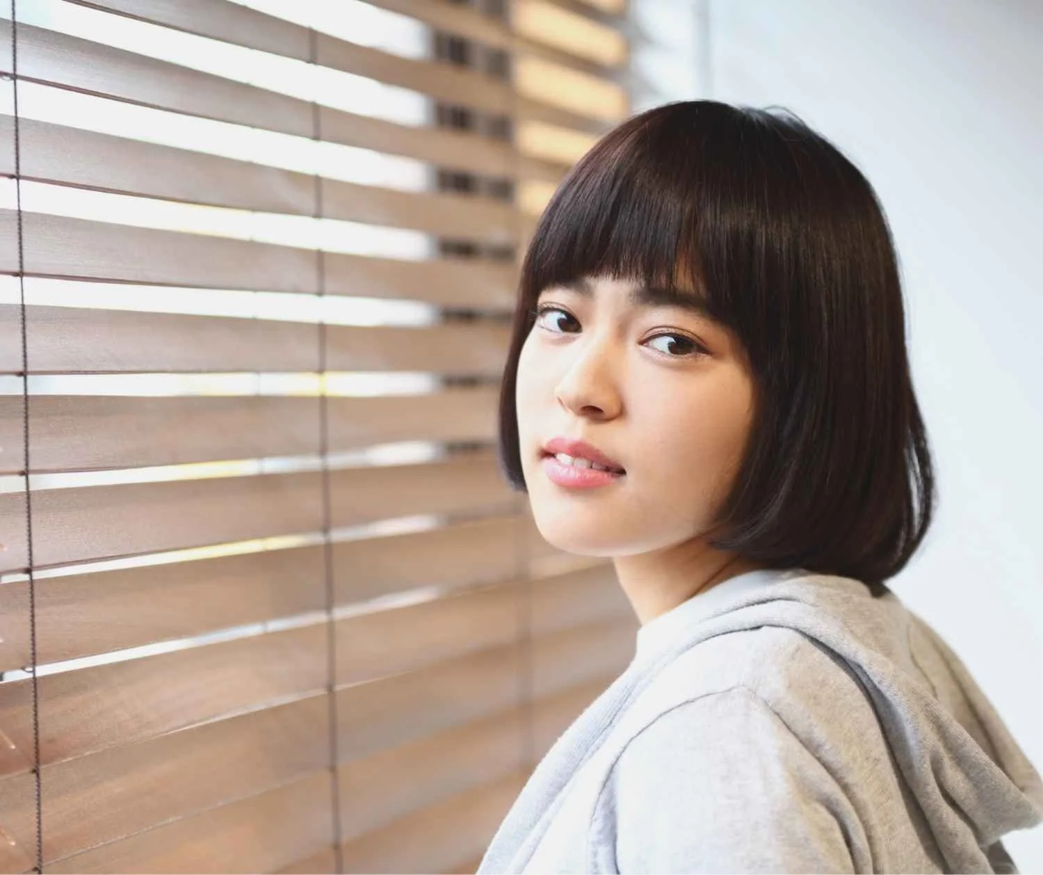 Young adult with short hair humming quietly by a sunny window.