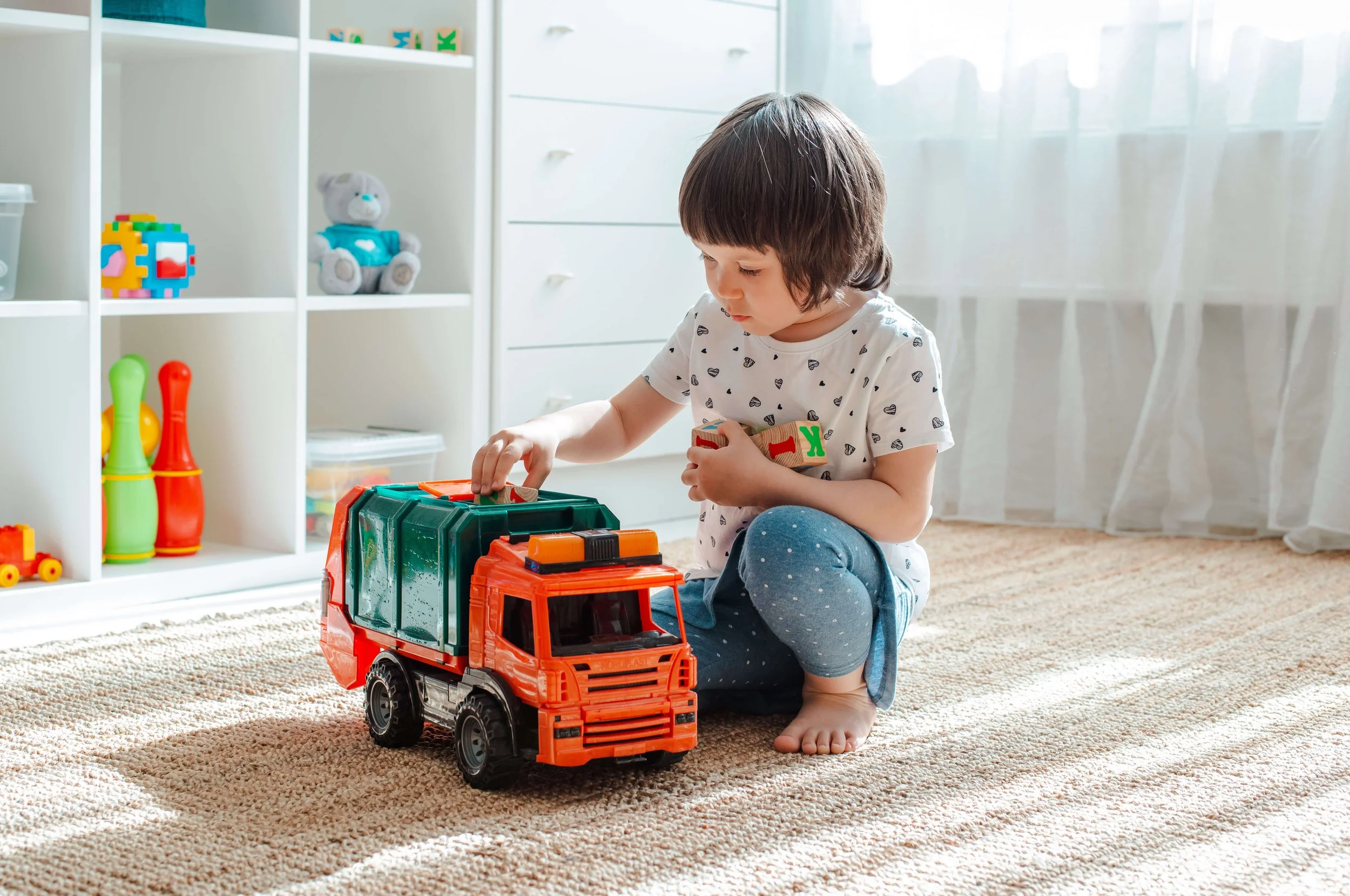 A toddler girl plays quietly with a dump truck